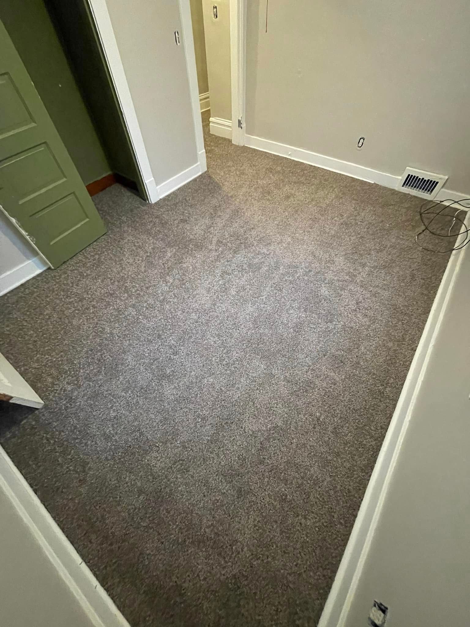 Room with gray speckled carpet, white trim, and a green door.
