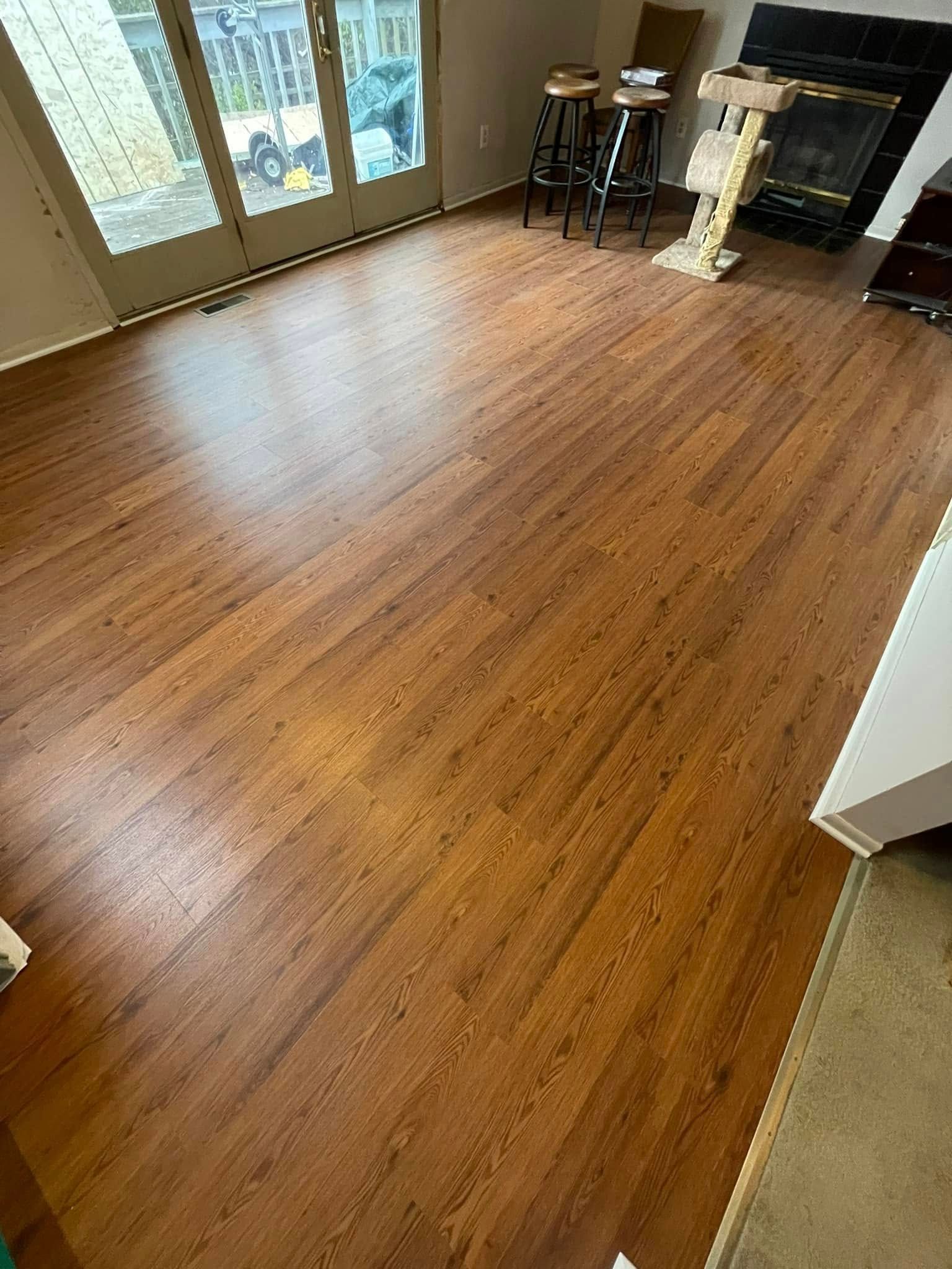 Brown wood-look flooring in a room with a fireplace, stools, and glass doors.