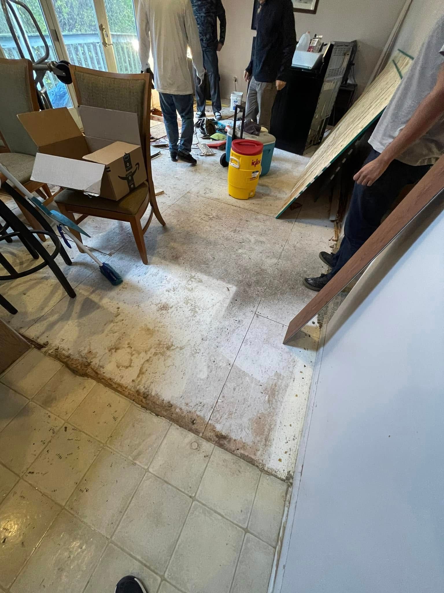 People standing in a room with debris and removed flooring.