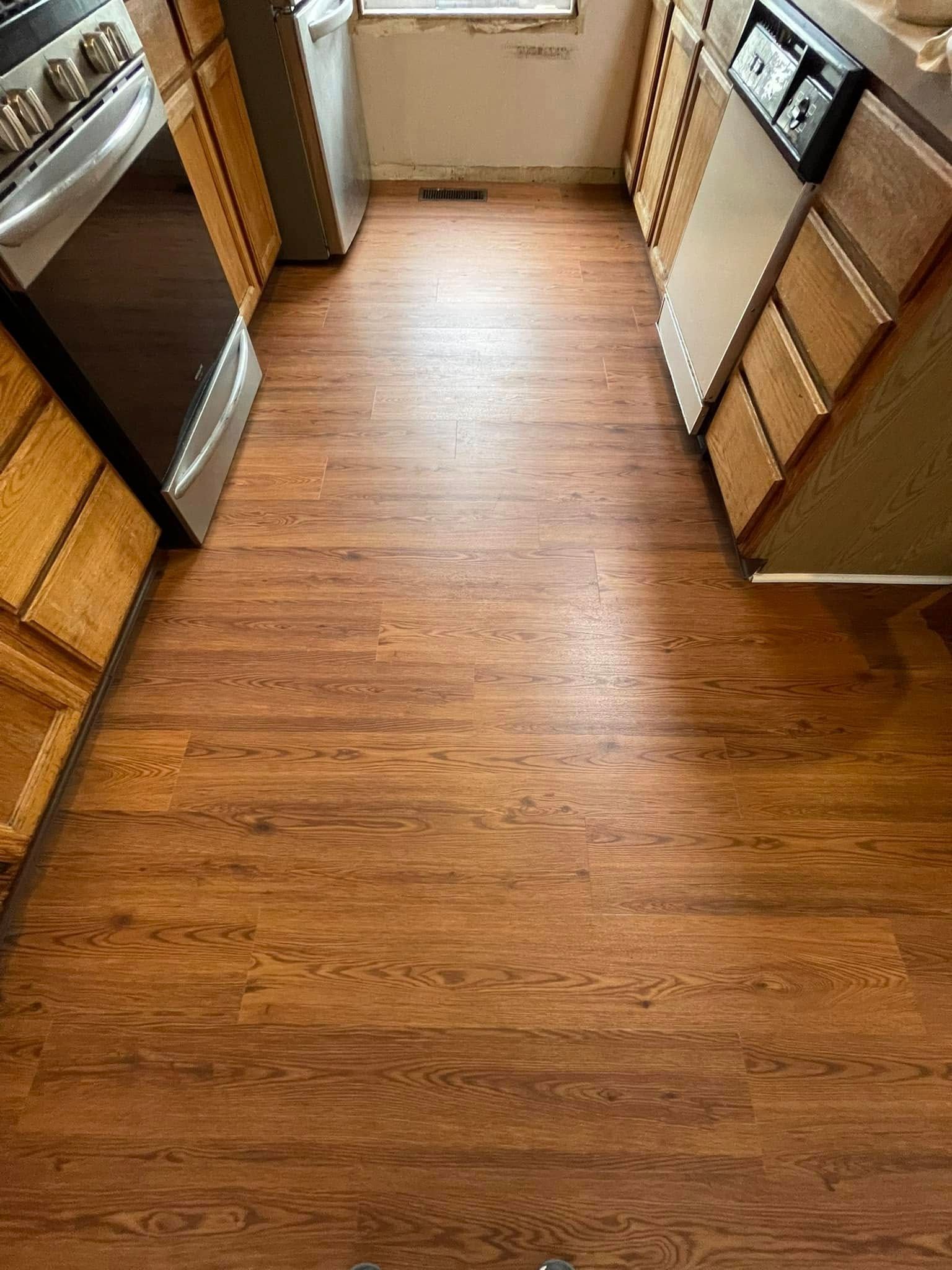 Kitchen with wood-look flooring and appliances along both sides: oven, dishwasher, and cabinets.