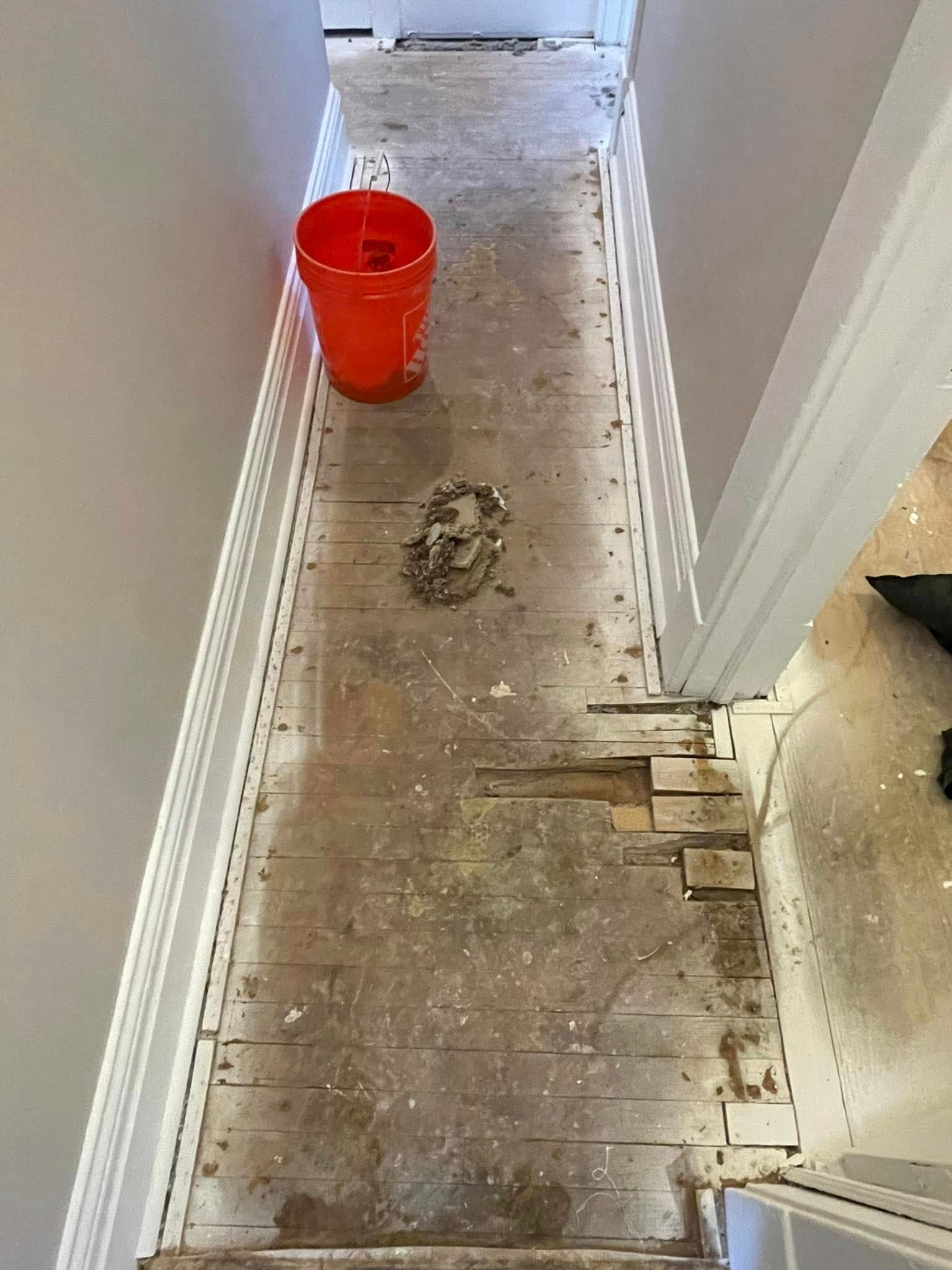 Narrow hallway with damaged flooring and orange bucket.