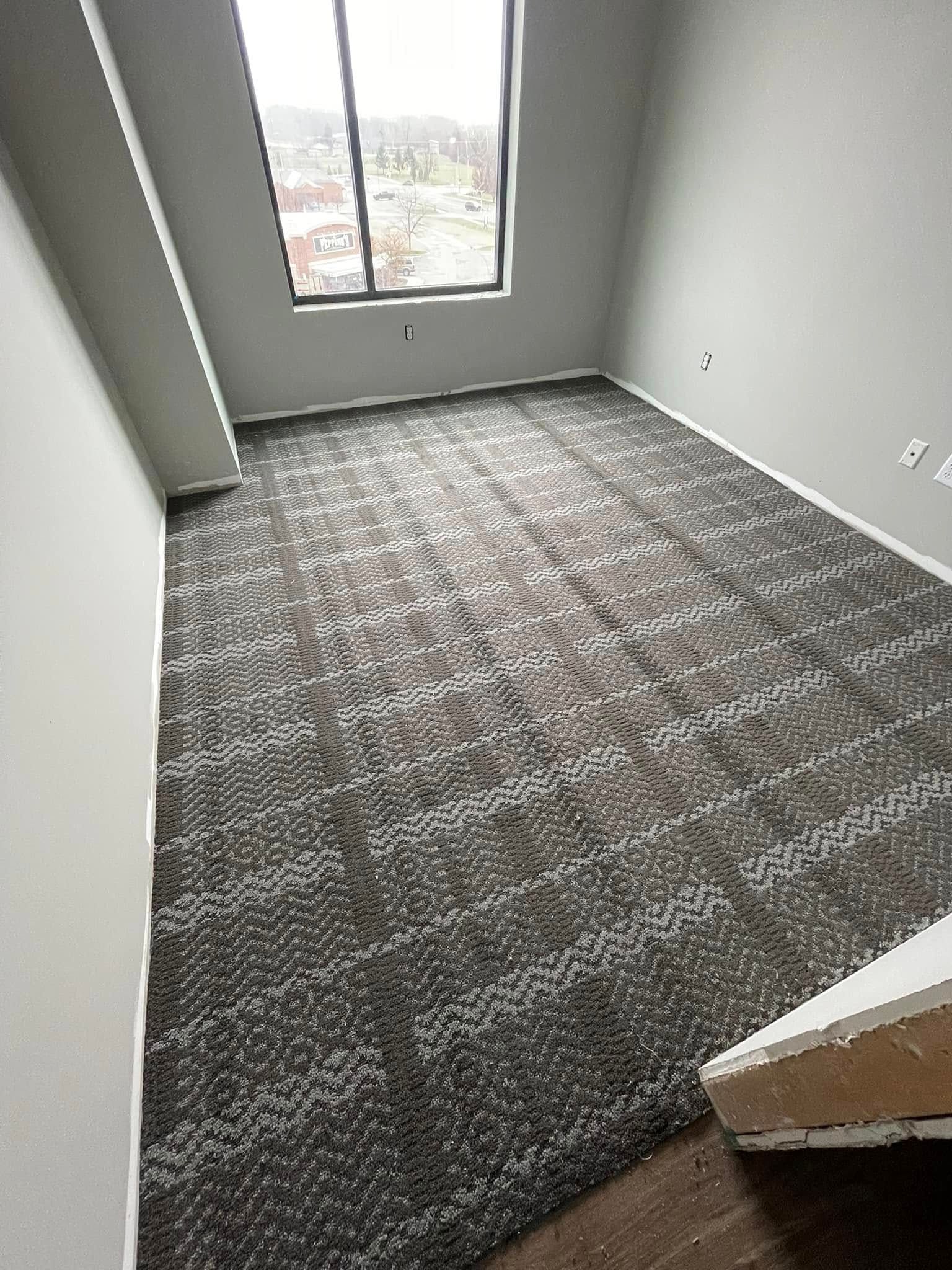 Empty room with gray walls and patterned carpet, window, and a door frame.