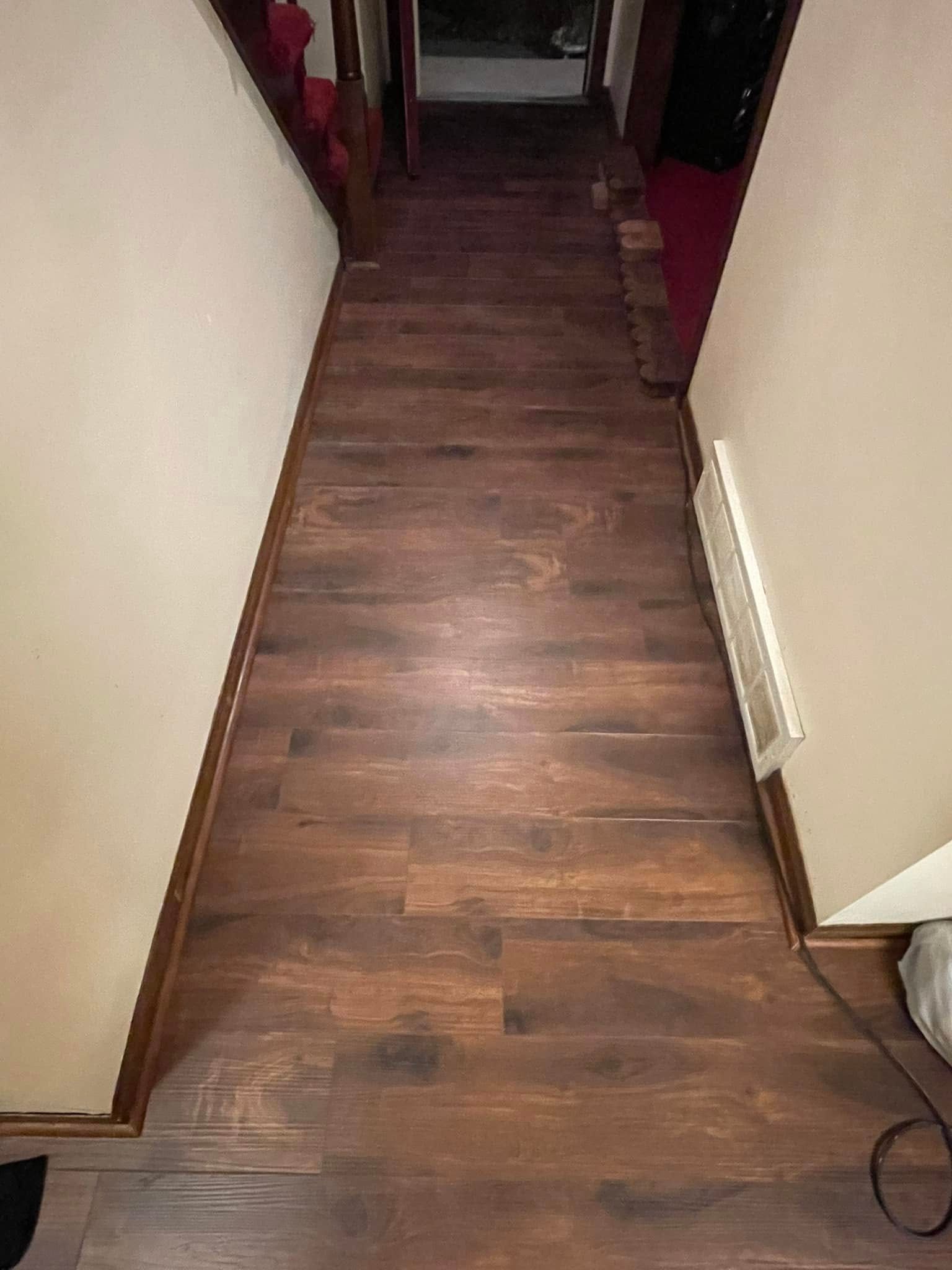 Wooden floor hallway with white walls and a glimpse of red carpet and stairs.