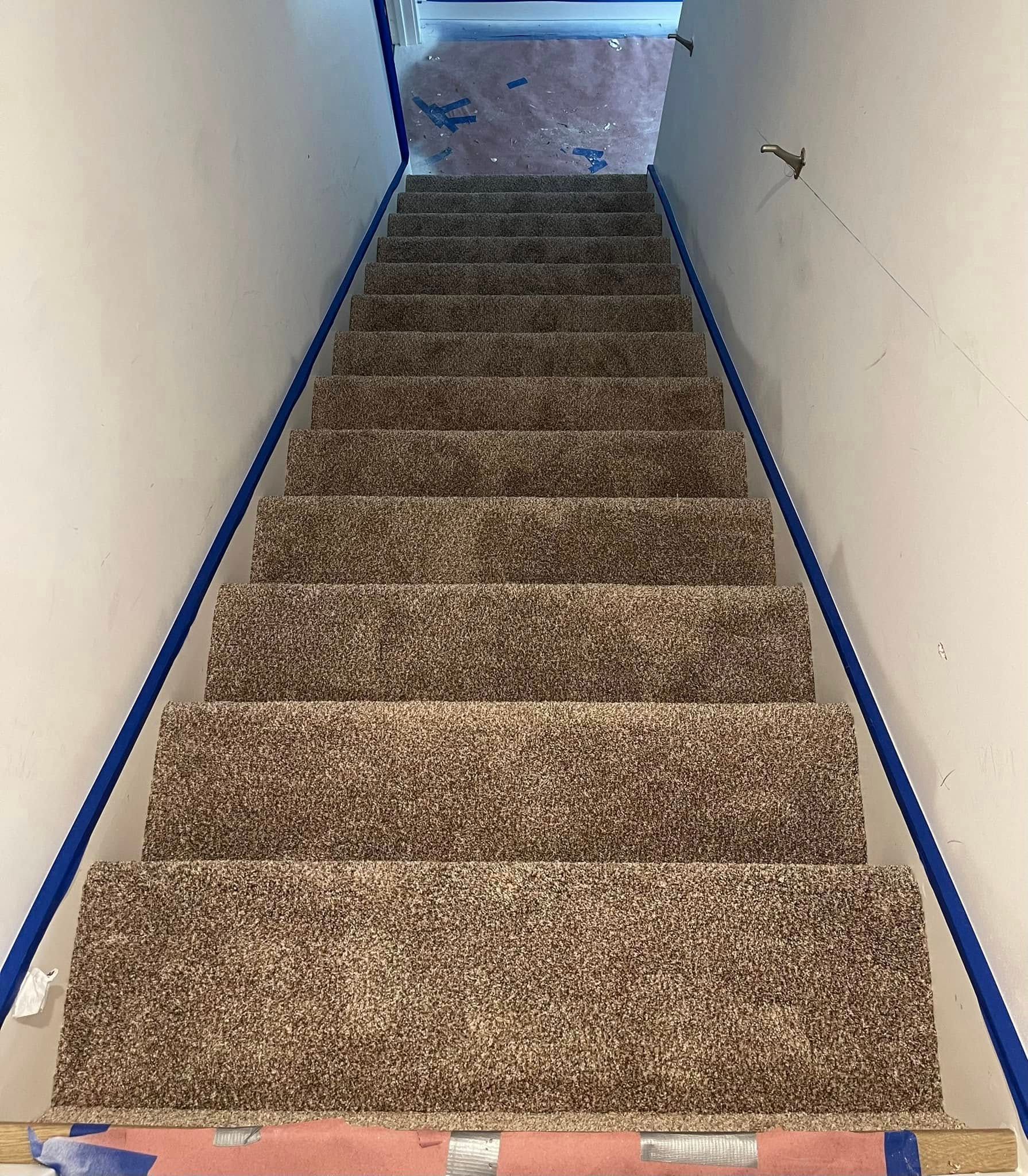 Staircase with brown carpet and white walls, blue painter's tape along the sides, leading upwards.