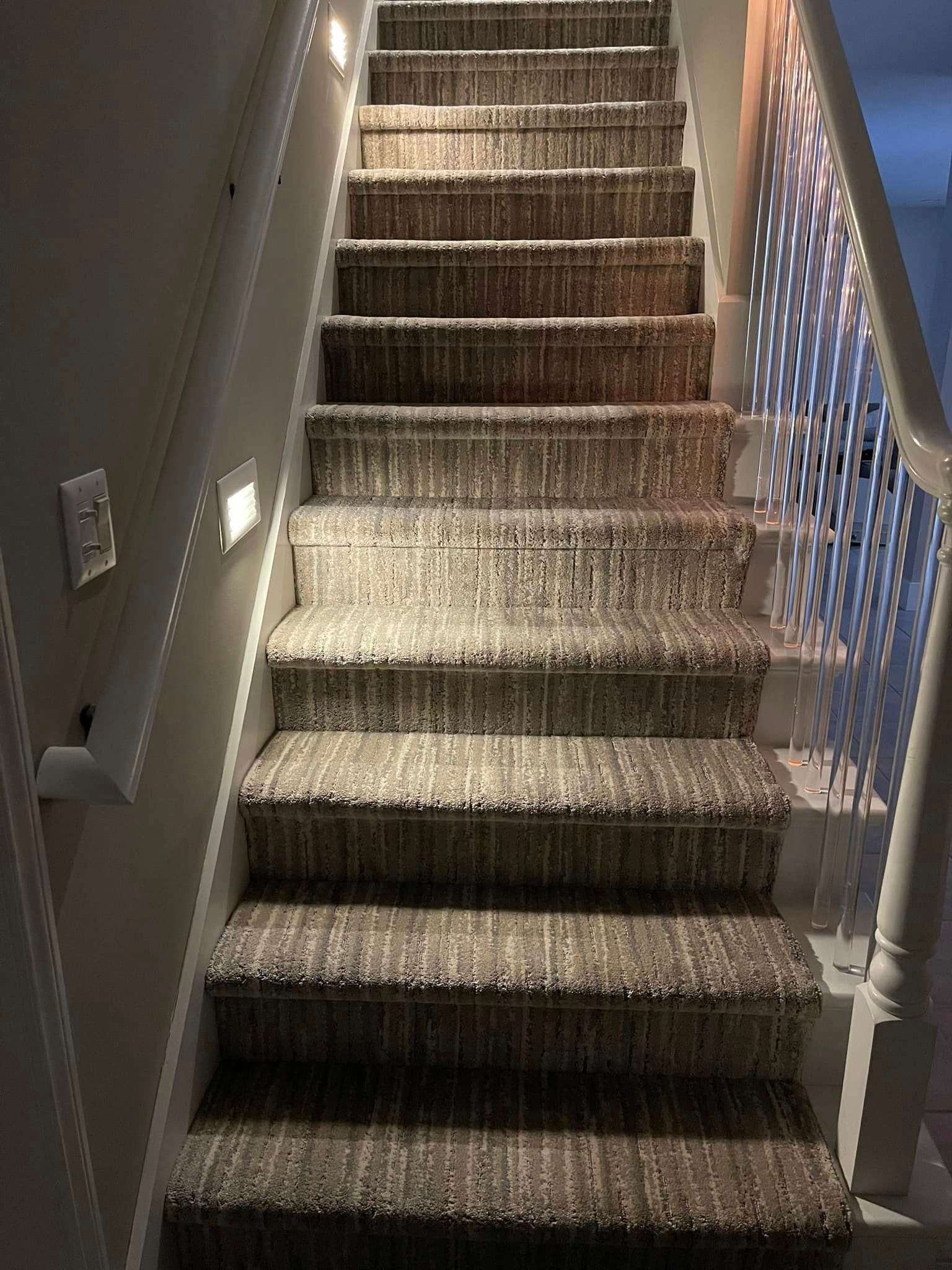 Carpeted staircase with recessed lighting along the wall and a white banister.