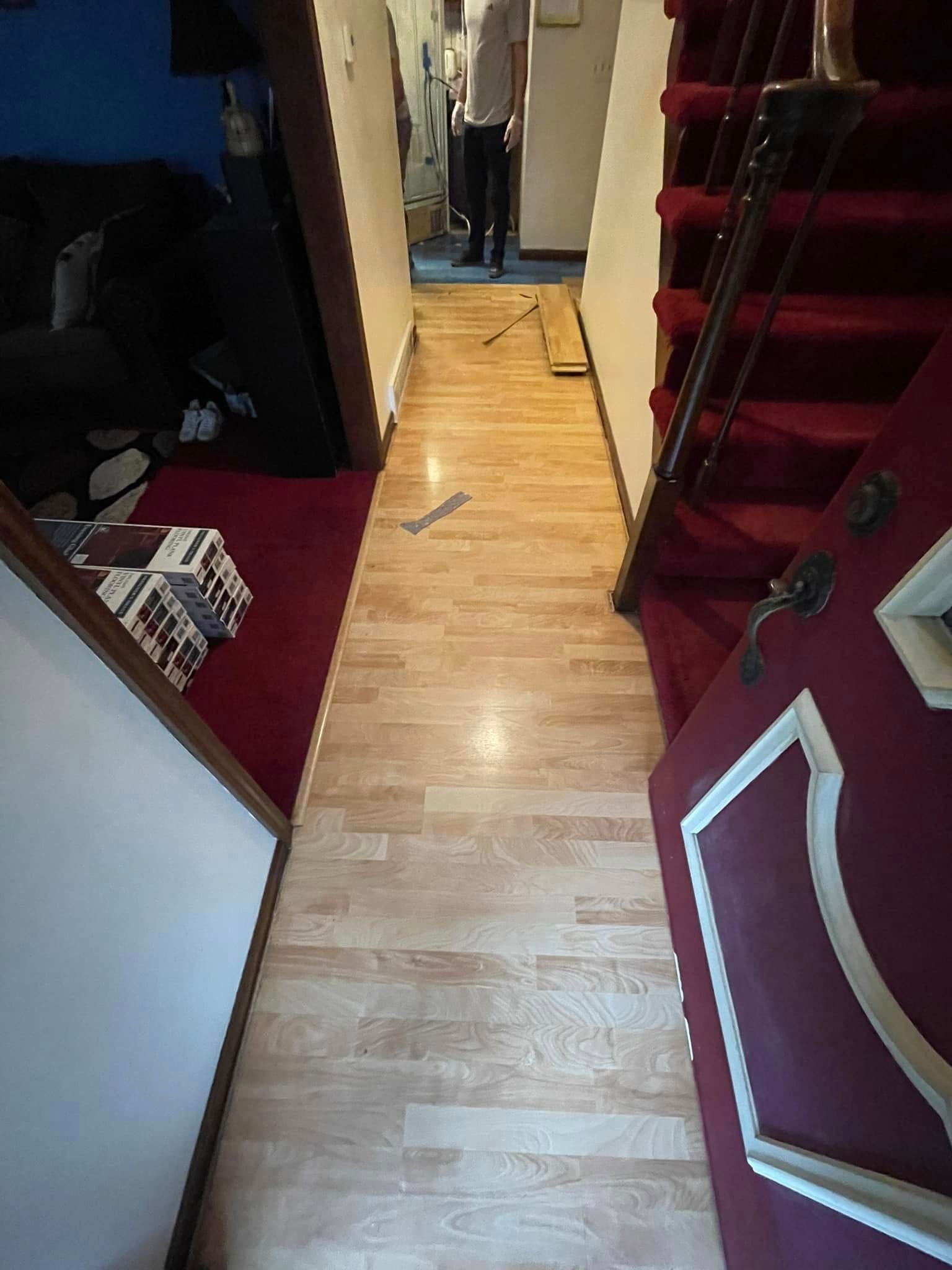 Hallway with light wood-look floor, red carpet on the sides and staircase. Person standing in the distance.