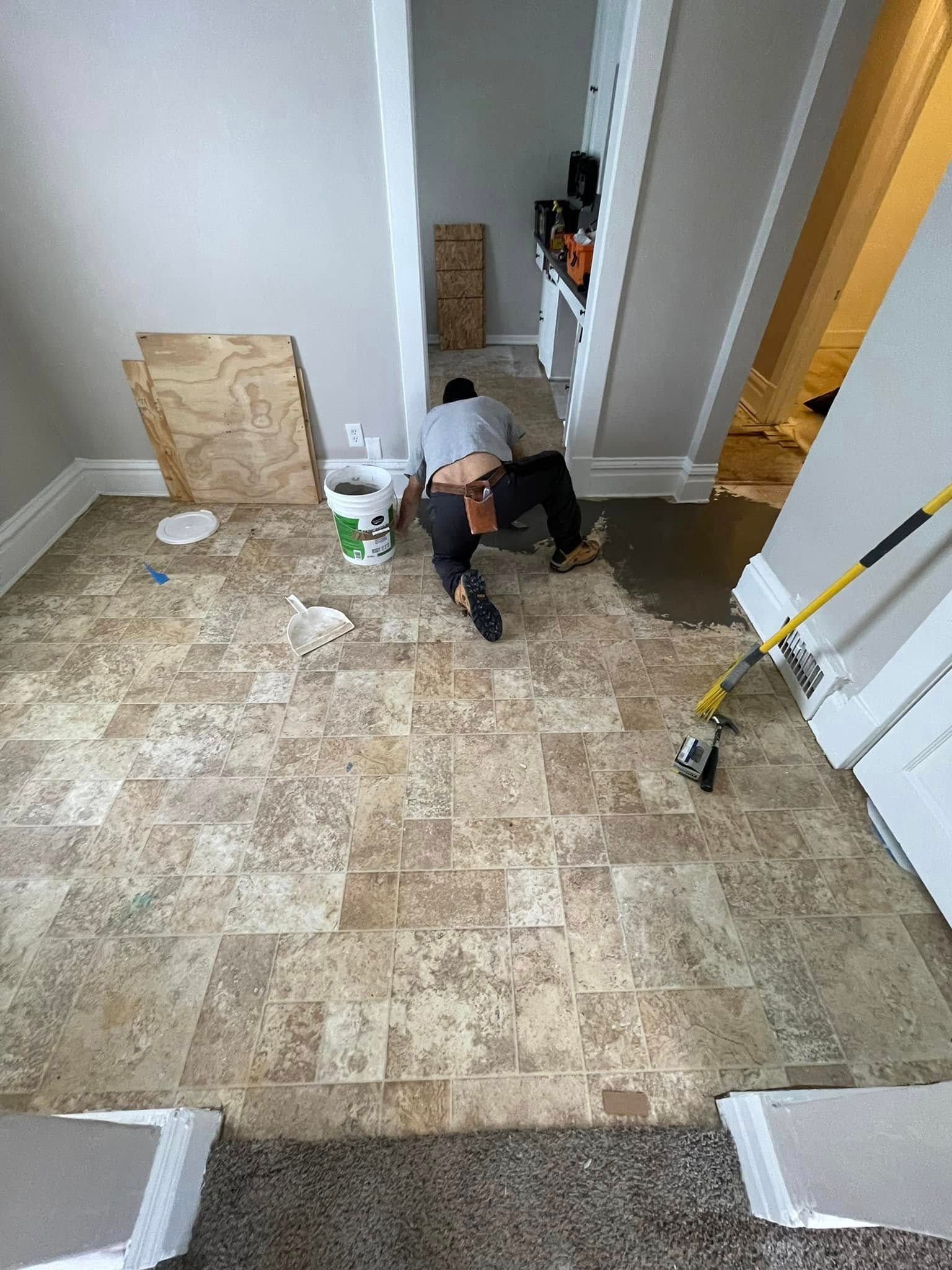 A person installing flooring in a room with light-colored walls and tan flooring.