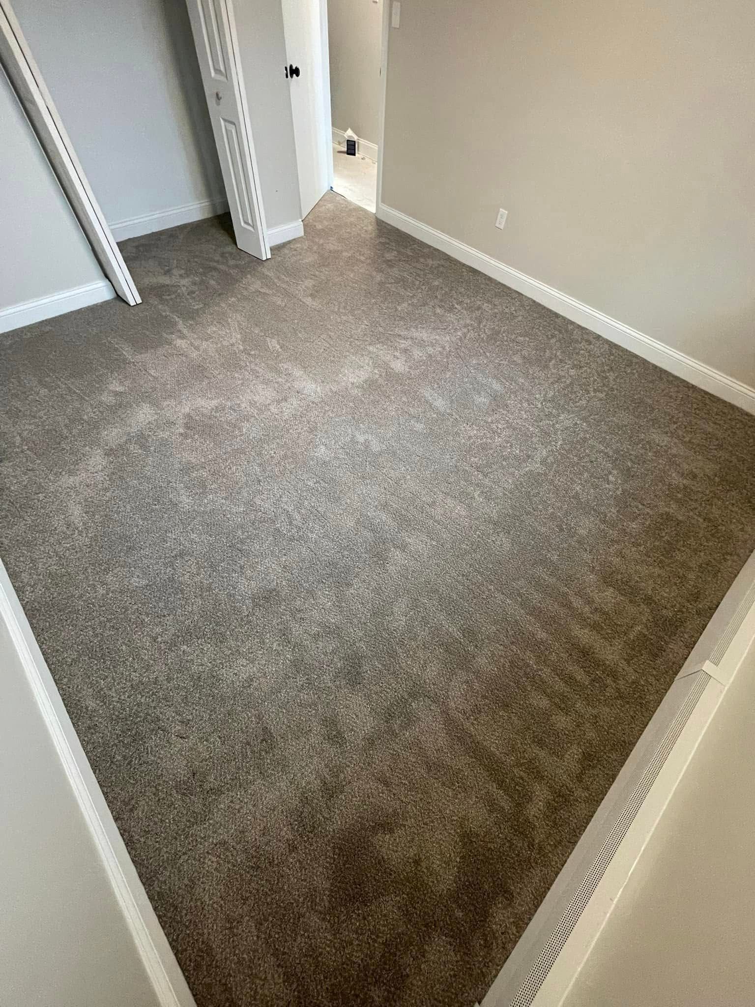 Empty room with new brown carpet and white baseboards.