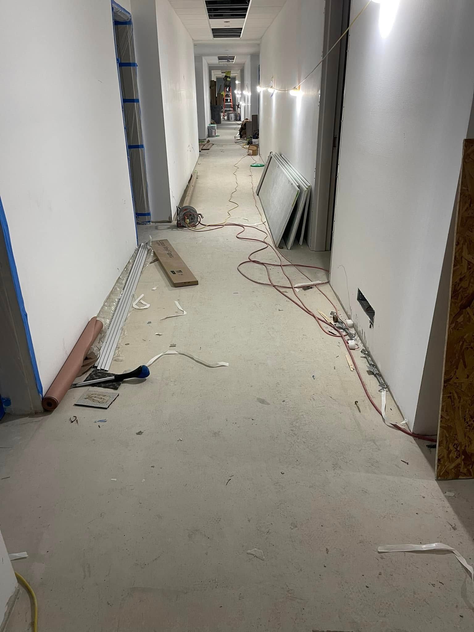 Construction site hallway with debris on the concrete floor, white walls, and overhead lighting.