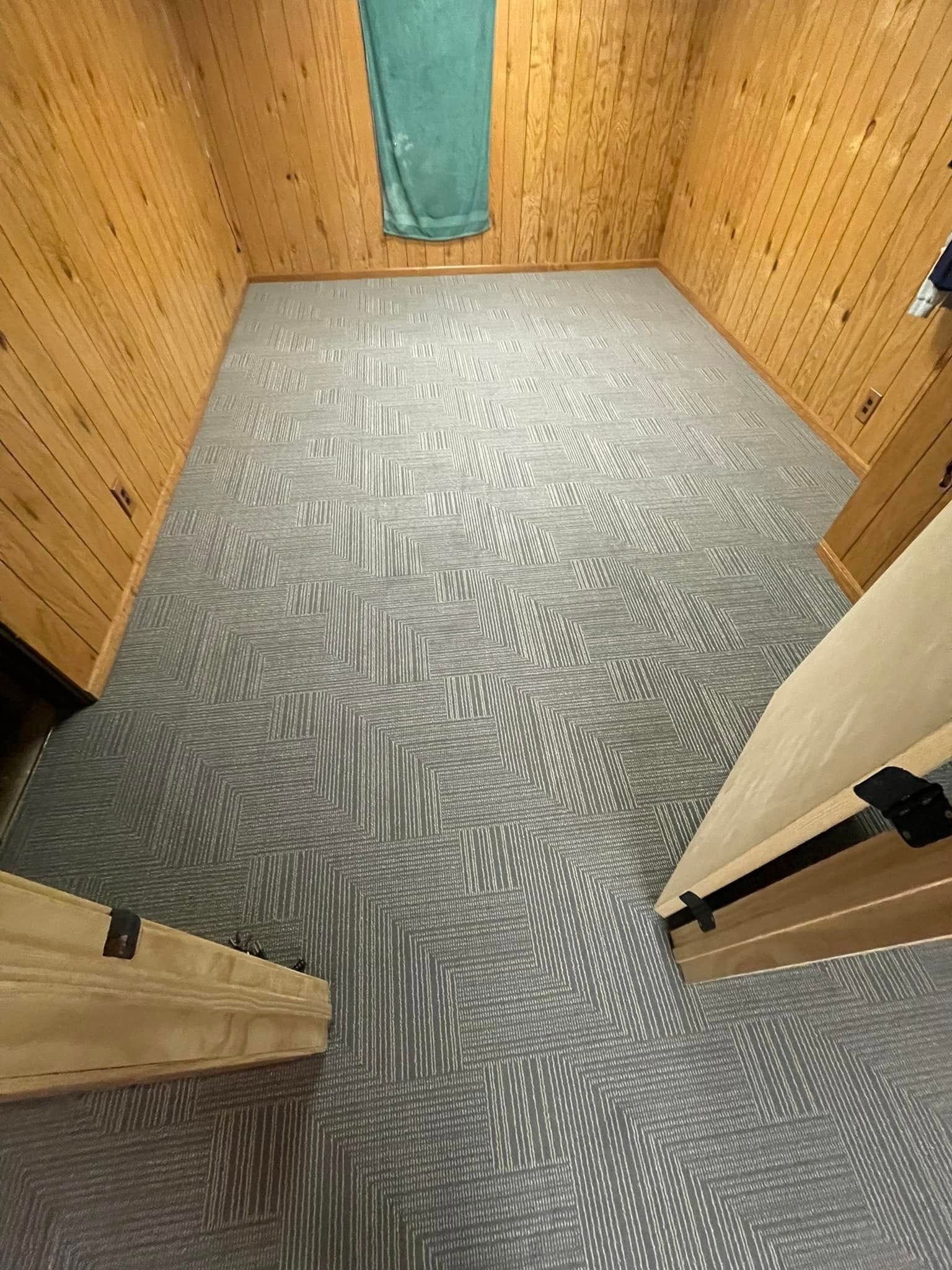 Wooden-walled room with patterned gray carpet, green towel, and sections of wooden structures.