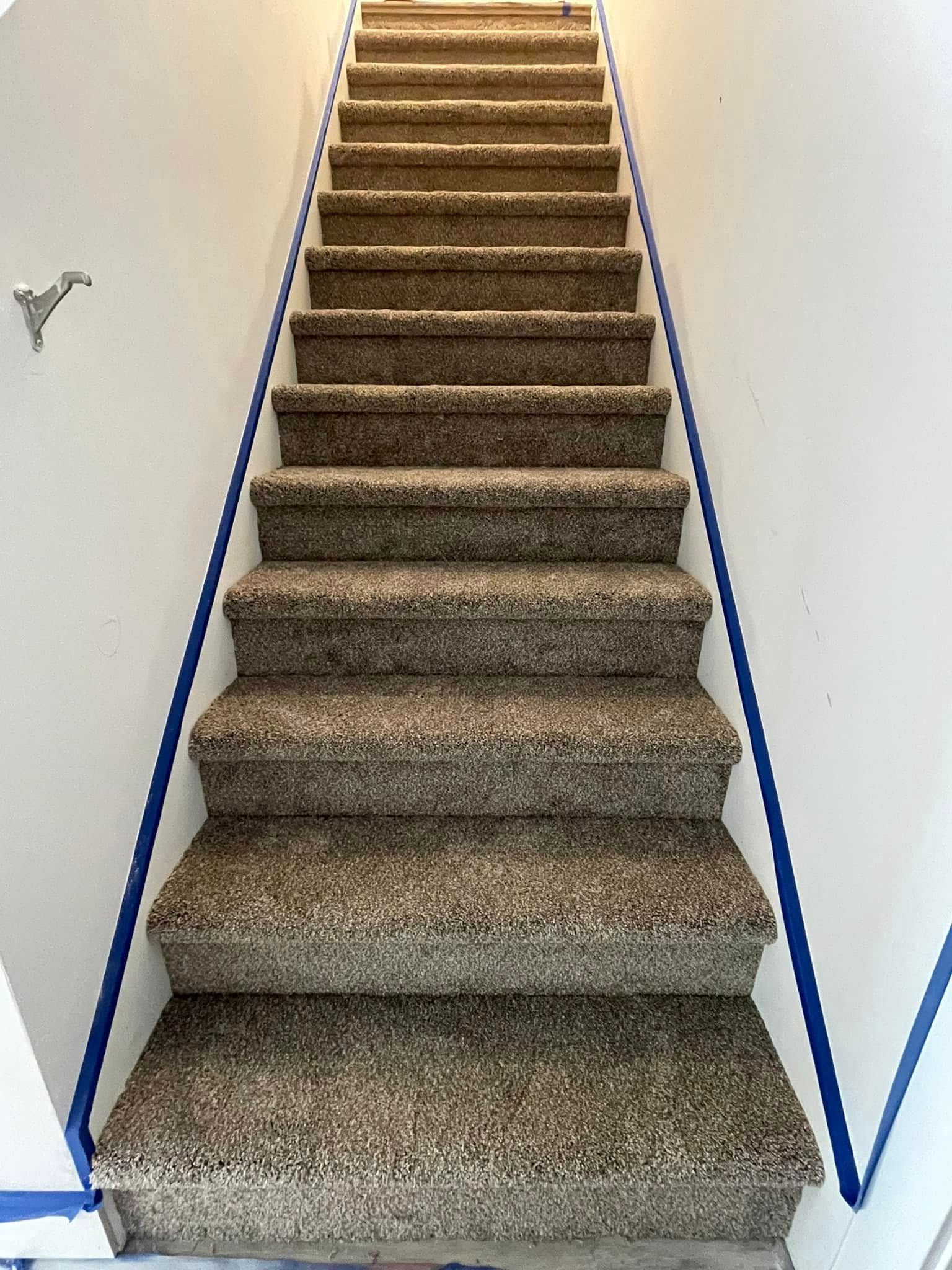 Staircase with carpeted steps leading upward, blue tape on walls, white walls.