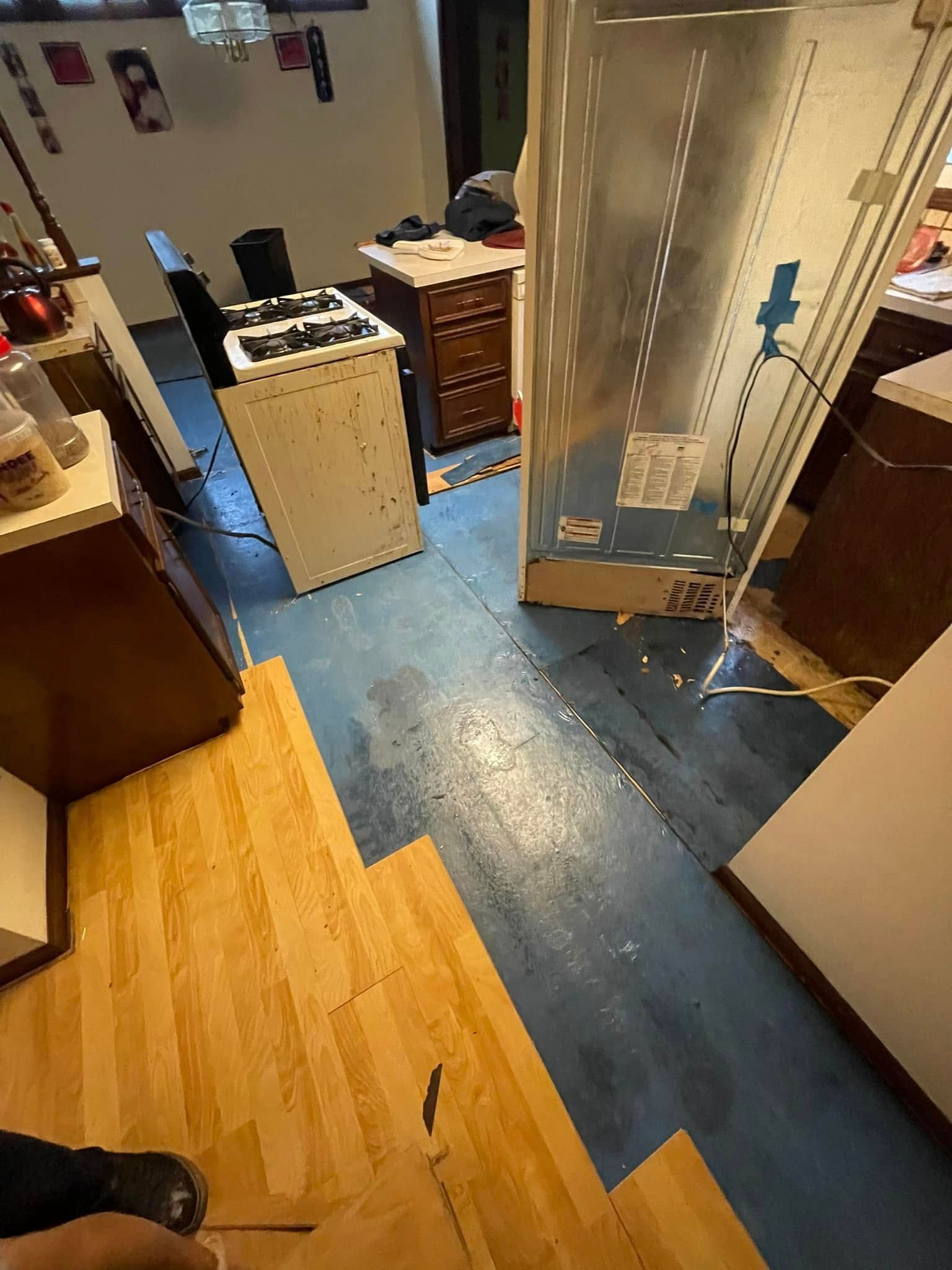 Kitchen with blue floor, partially covered by wood-look laminate flooring. Appliances and cabinets are visible.