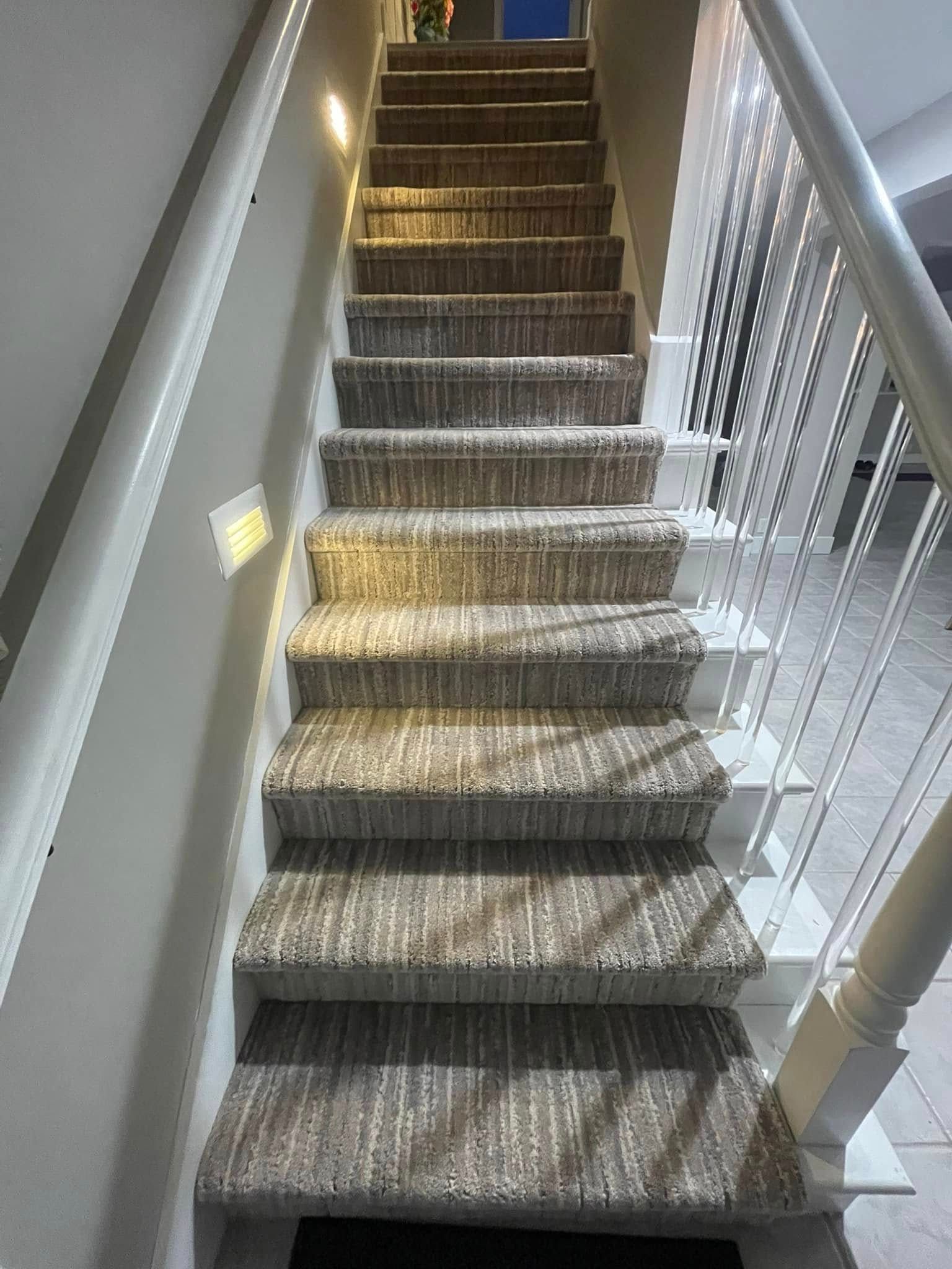 Carpeted staircase with white balusters and handrails, lit by recessed lights.