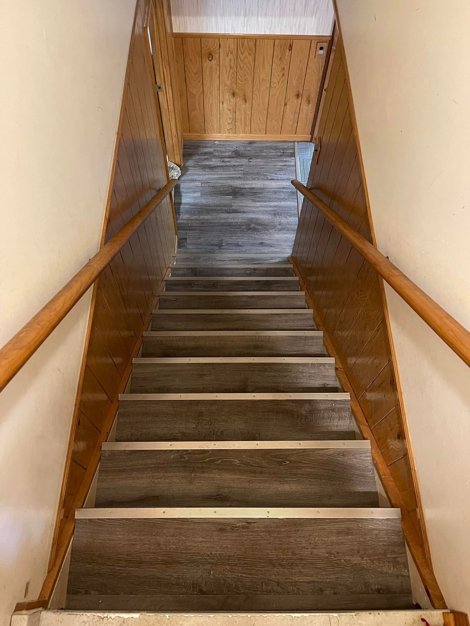 Wooden staircase leading upward, brown handrails and side panels with a neutral-colored wall on either side.