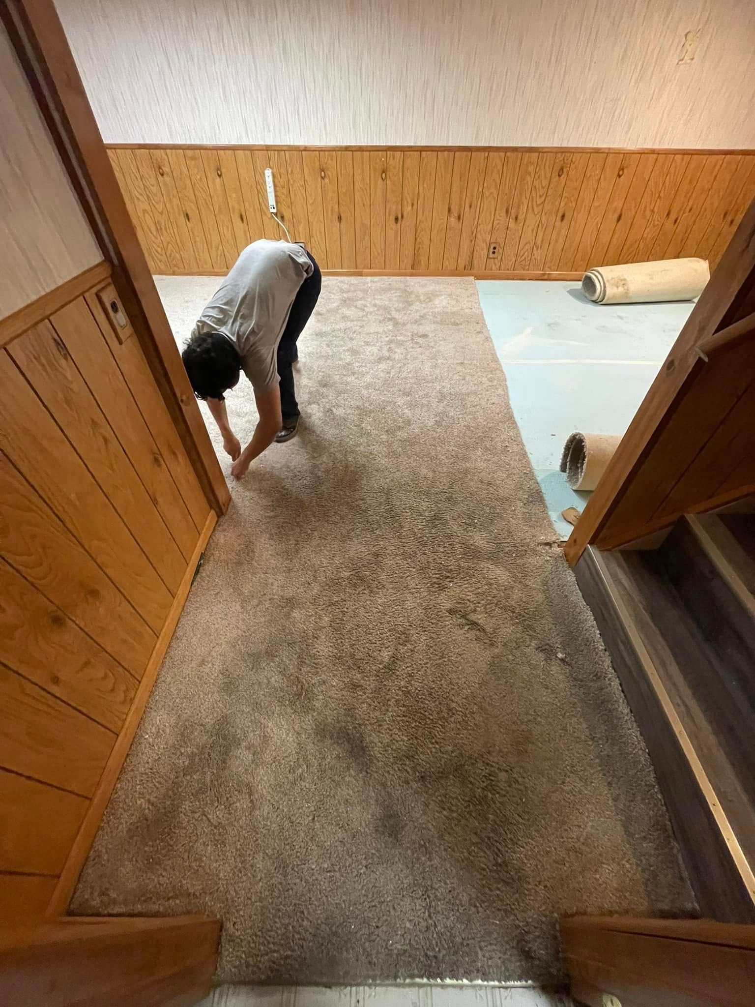 Person bending over a carpeted area between stairs. Beige carpet, brown wood walls and stairs.