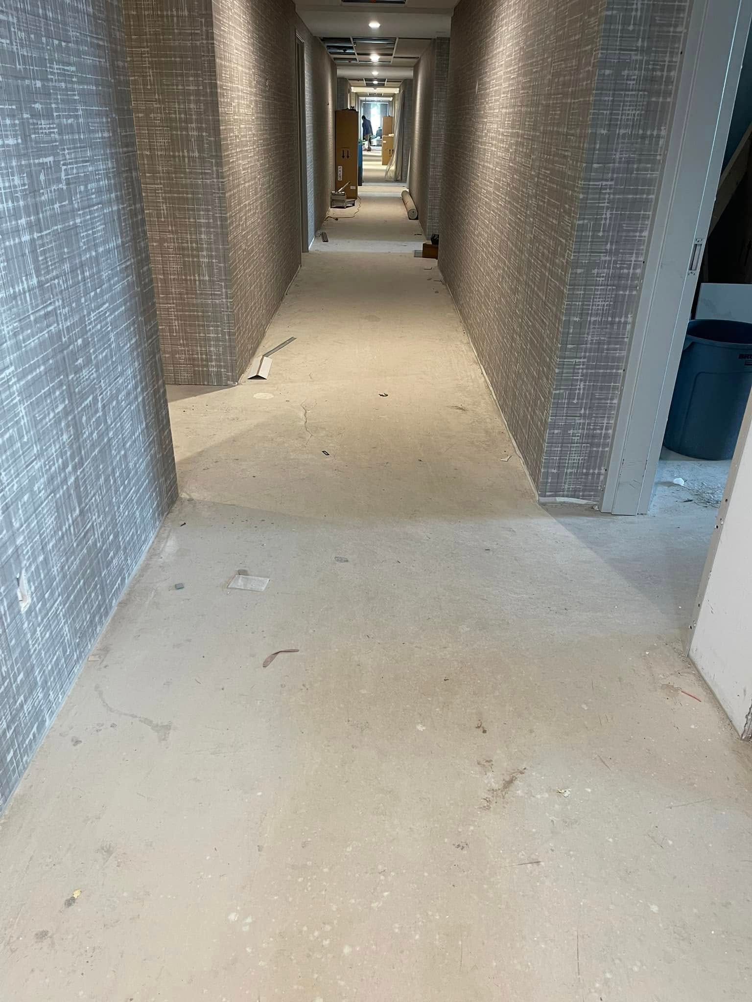 Construction in a long hallway, walls with brickwork, concrete floor, leading to a doorway at the end.