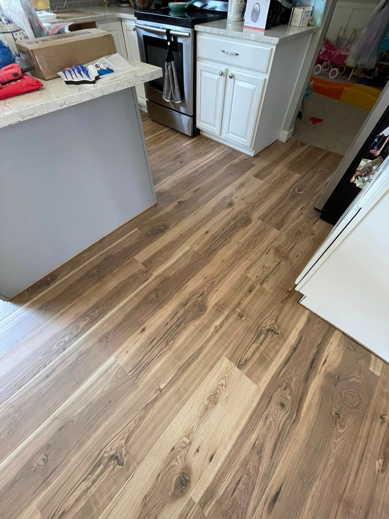 Wood-look flooring in a kitchen with a white island and cabinets, and a stainless steel stove.