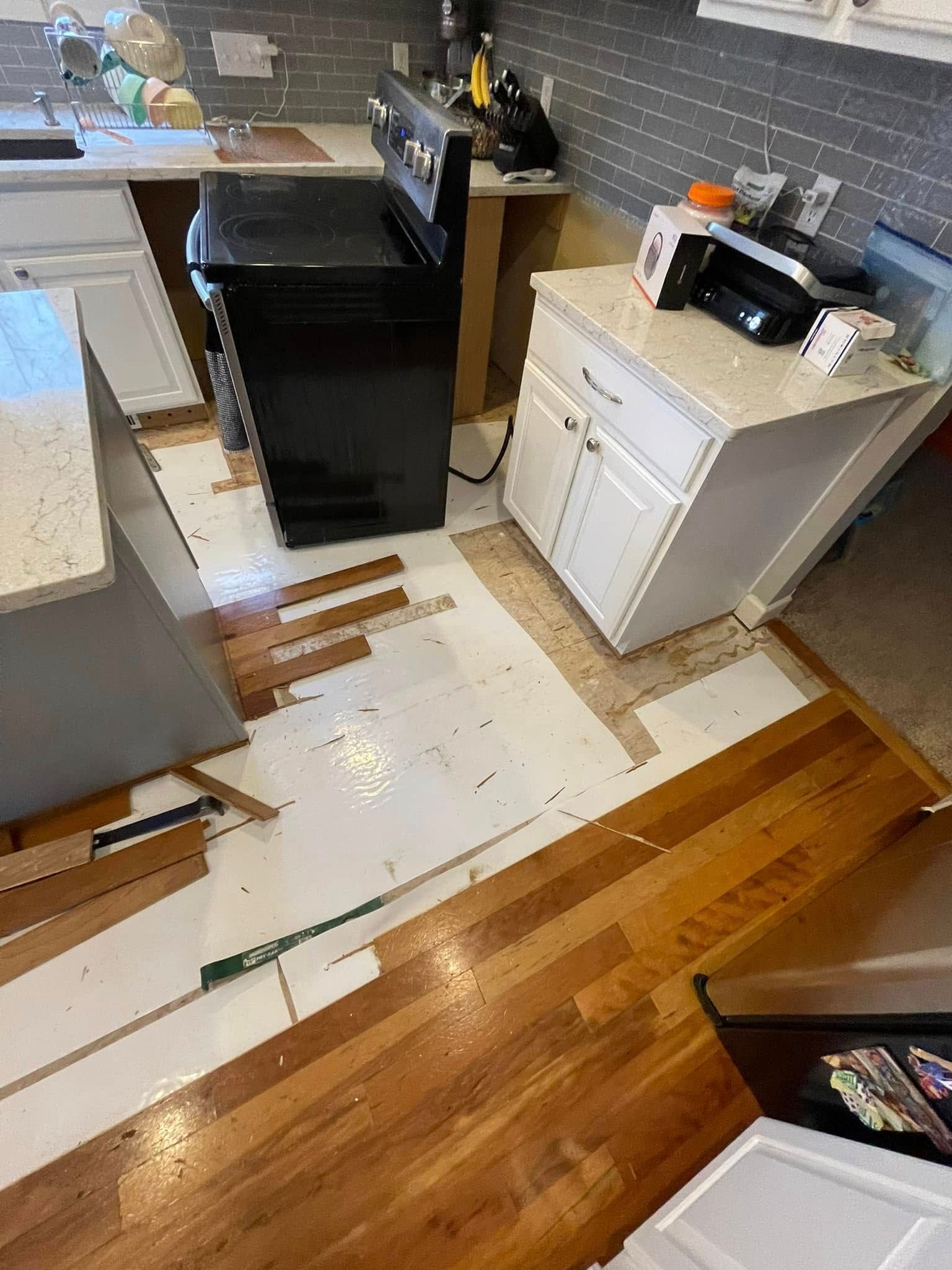 Kitchen renovation: hardwood floor partially removed, exposing subfloor; stove and cabinet in place.