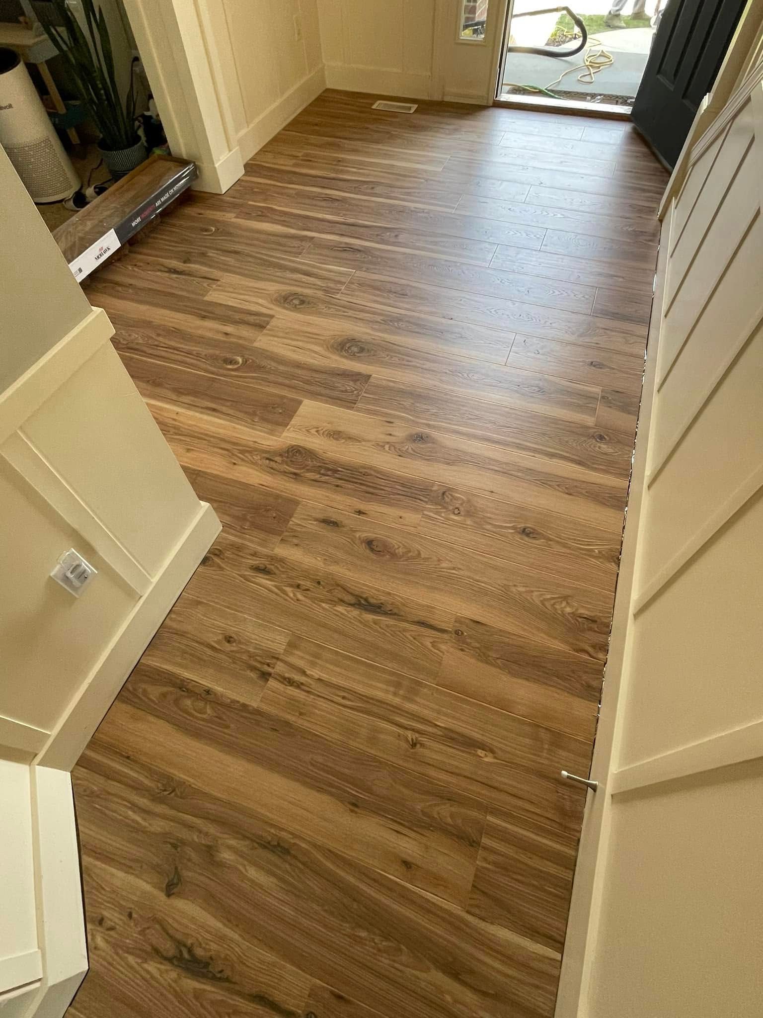 Wooden plank flooring in a hallway with a door to the outside. Cream-colored trim lines the walls.