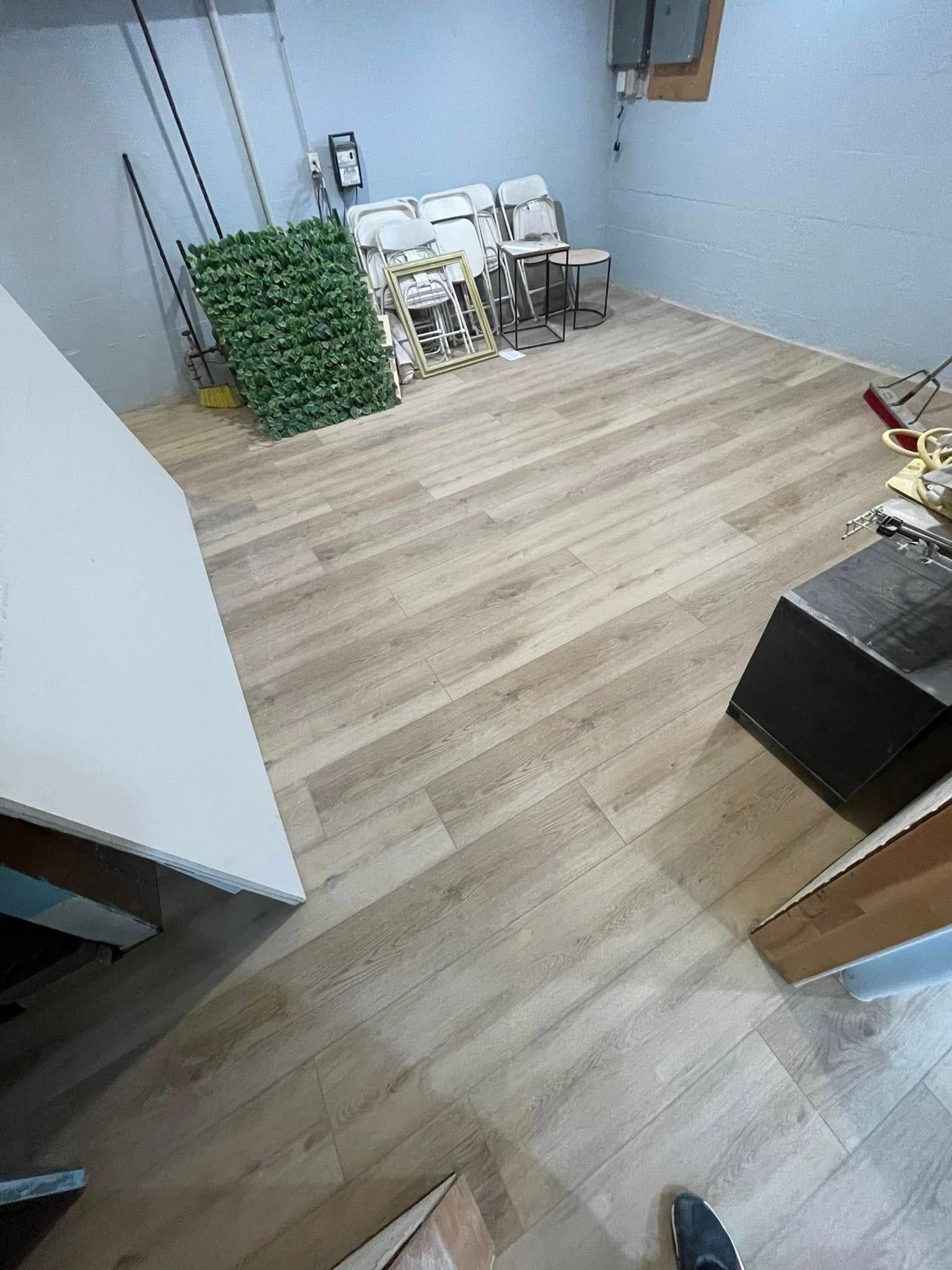 Room with new light wood-look flooring and stacked supplies against light blue walls.