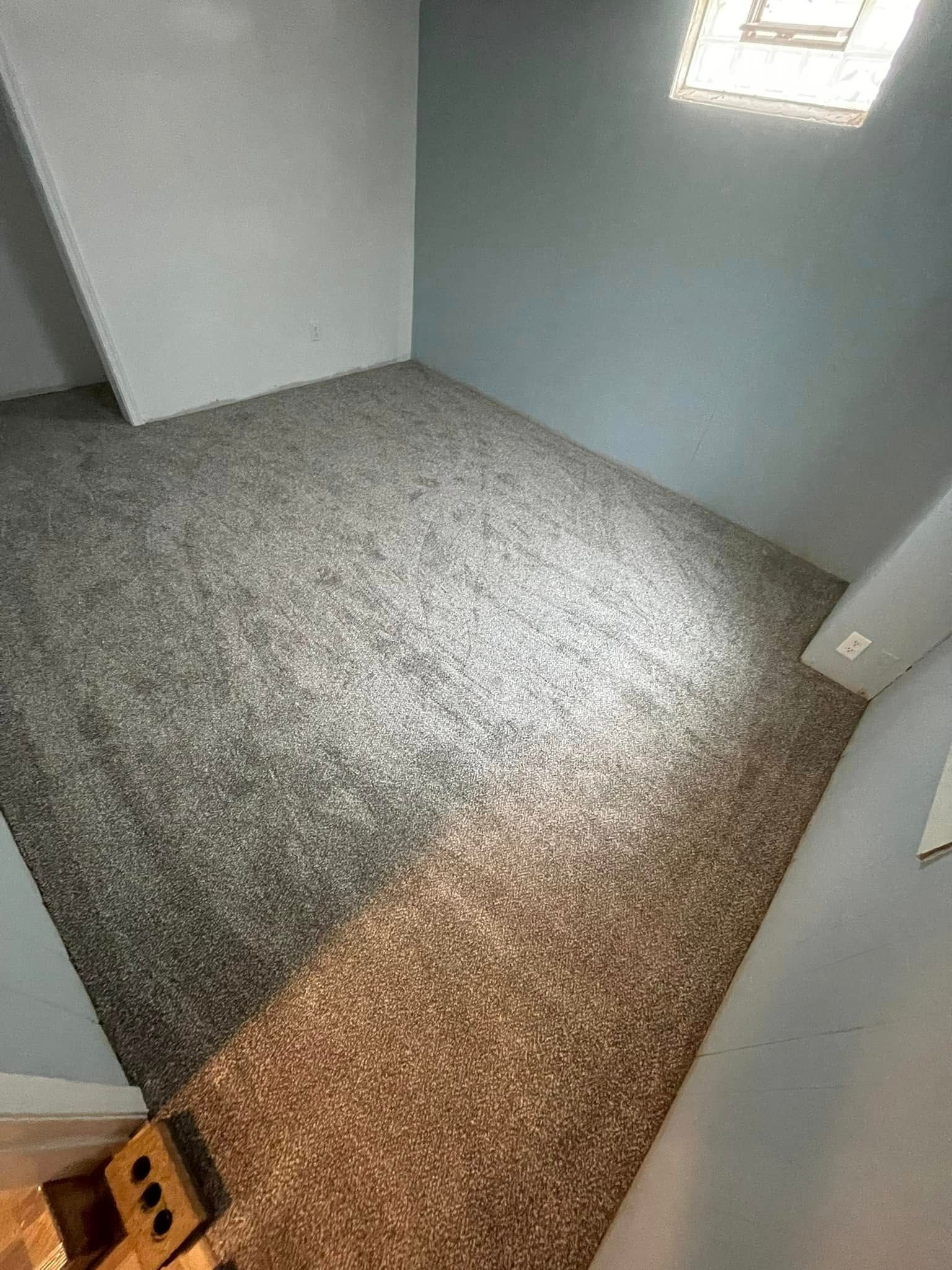Room with new gray and brown speckled carpet; light blue and white walls; small window.