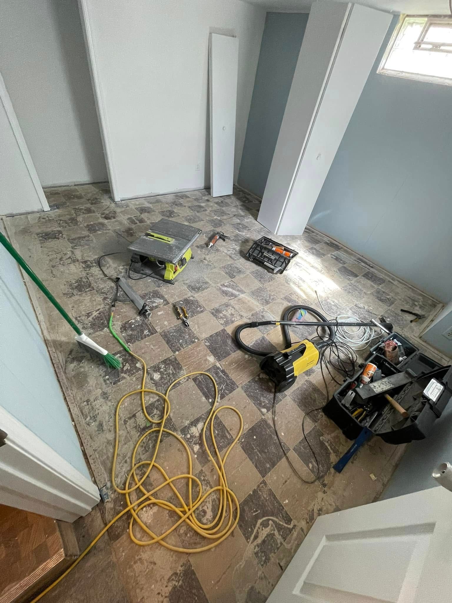 Room under renovation: exposed floor, tools, blue and white walls, door, and a coiled yellow cord.