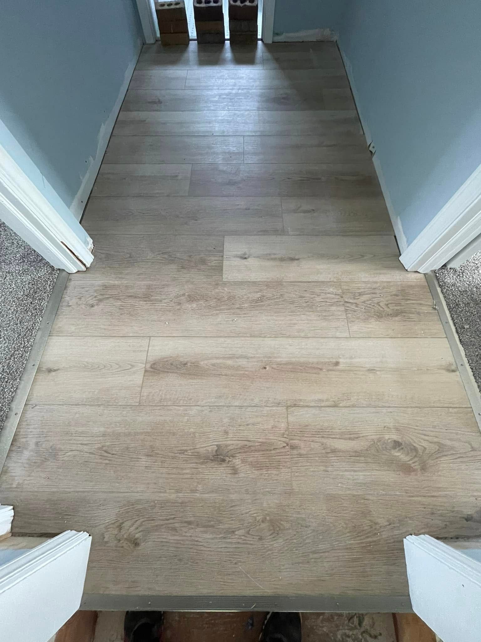 Hallway with wood-look flooring. Light brown planks, bordered by doorways with white trim. Carpet on either side.