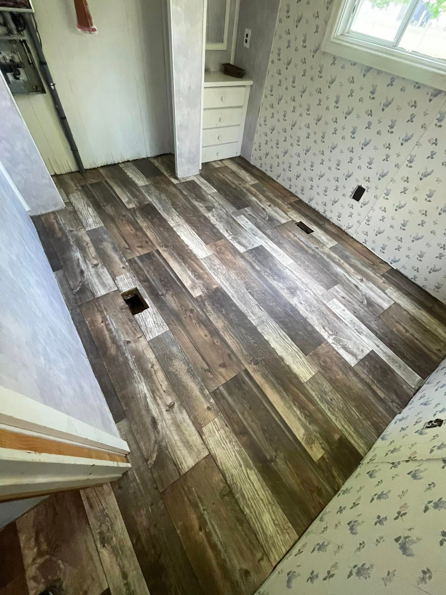 Wood-look flooring in a room with patterned wallpaper, a doorway, and a small window.