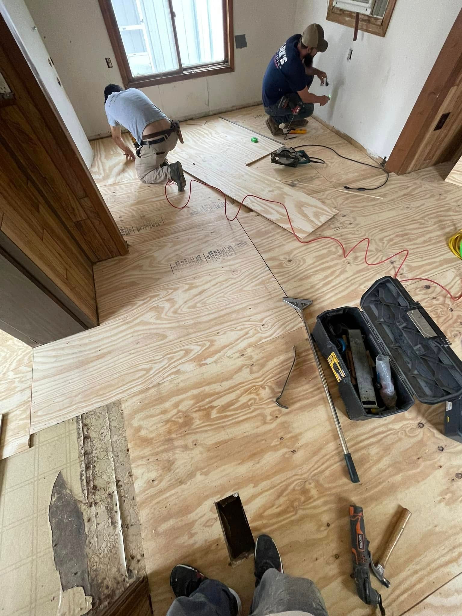 Two people installing a wood floor in a room. Tools and wood scattered around.