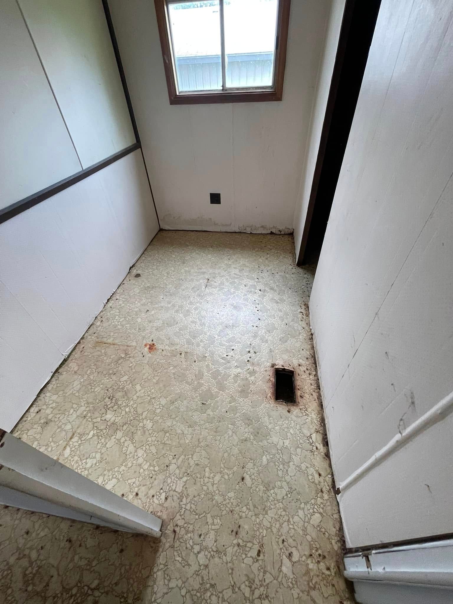 Small room with window, linoleum floor, and air vent. Walls are white and partially paneled.