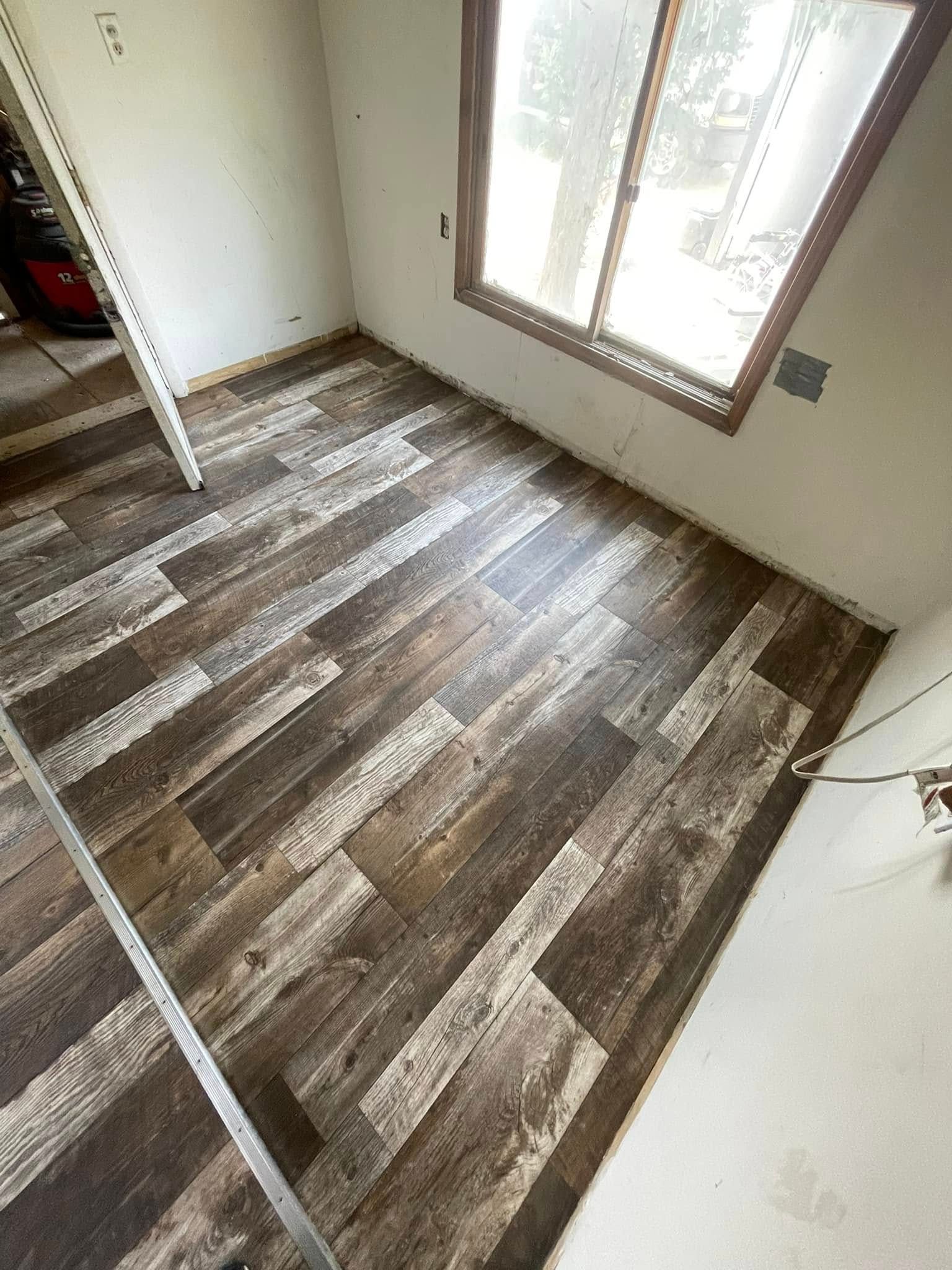 Newly installed wood-look flooring in a room with a window. The walls are white and the floor is a mix of brown and light wood tones.