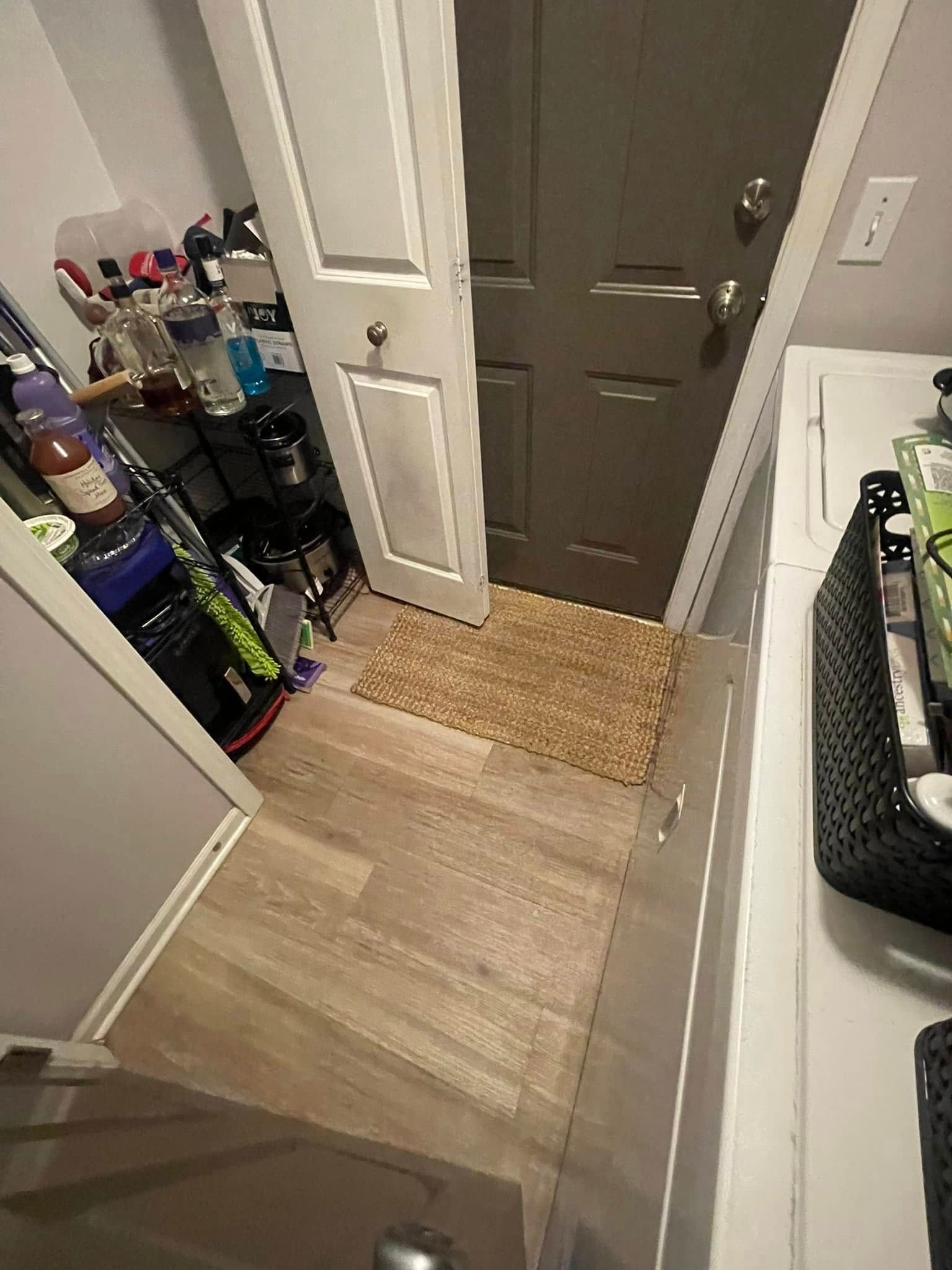 Narrow entryway with door, rug, shelving with items, and laundry machine.