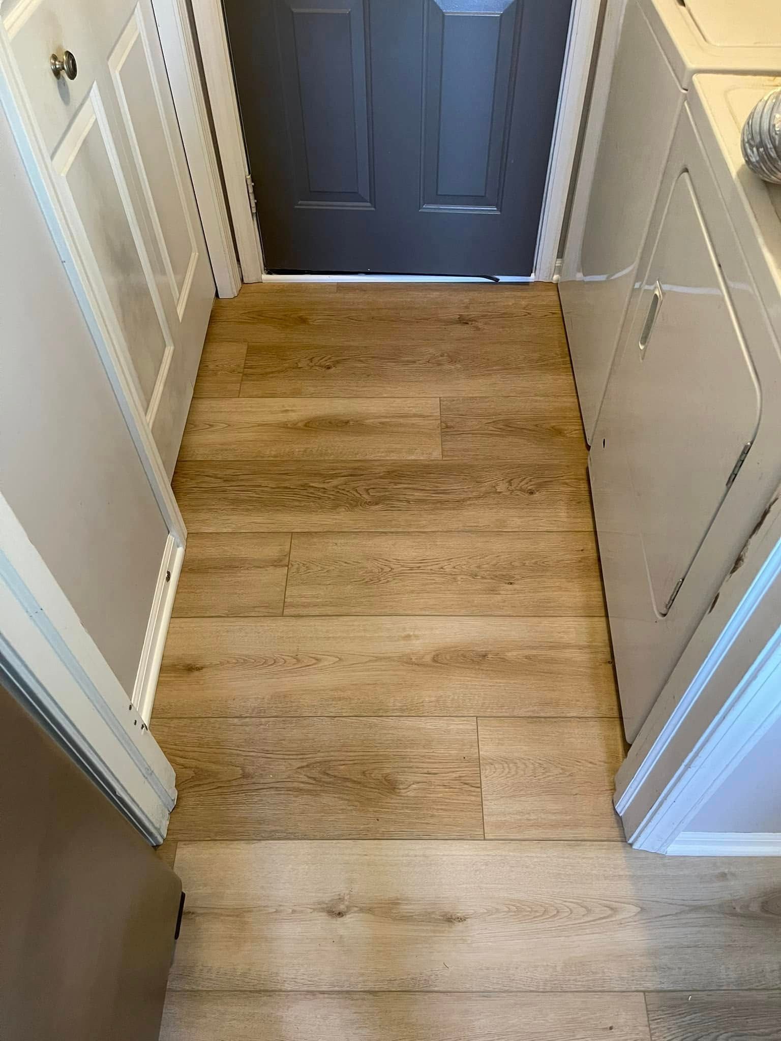 Narrow entryway with light wood-look floor, framed by white cabinets. A dark gray door is at the end.