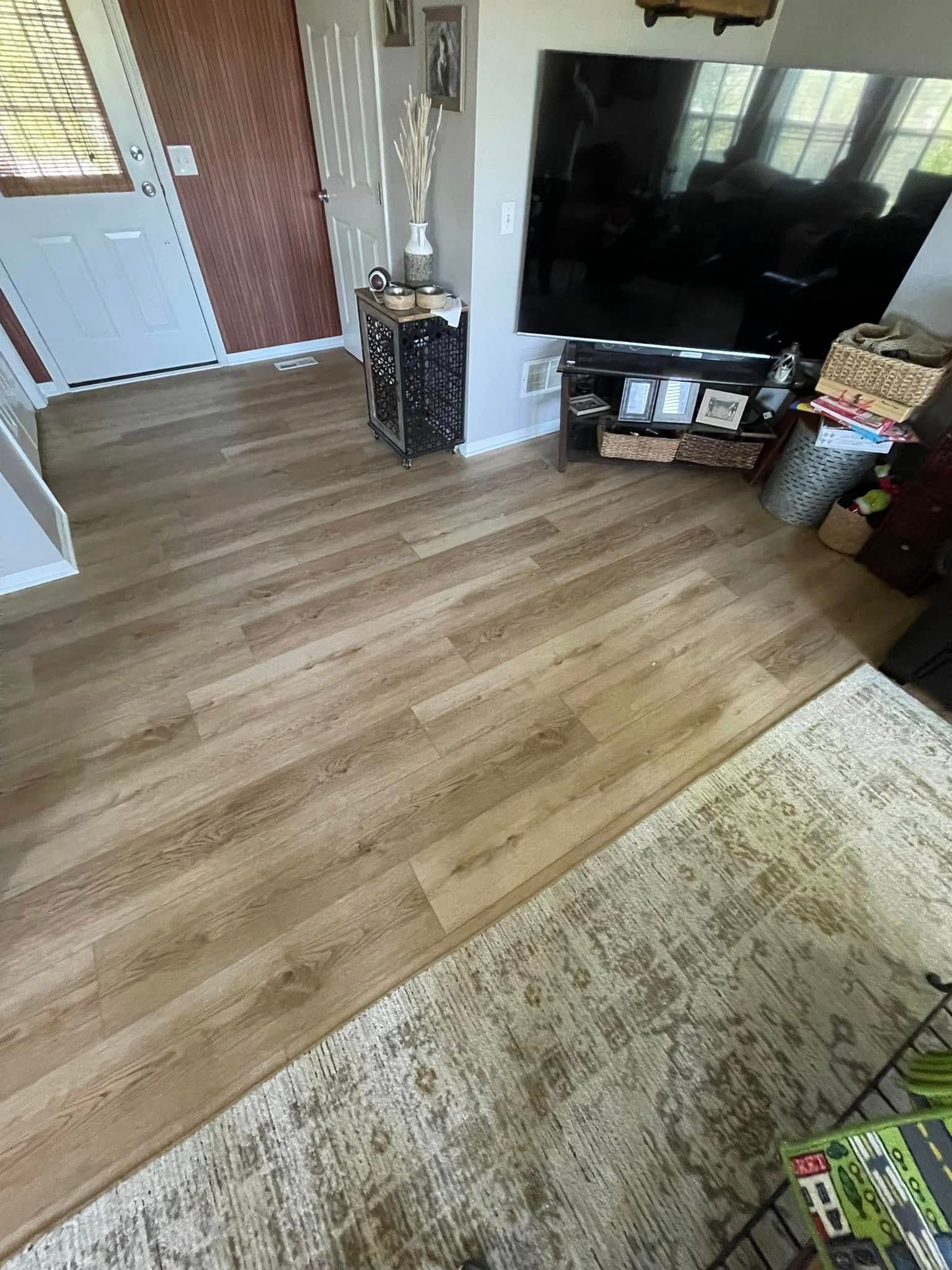 Wooden floor in living room with rug, TV, door, and decorative items.
