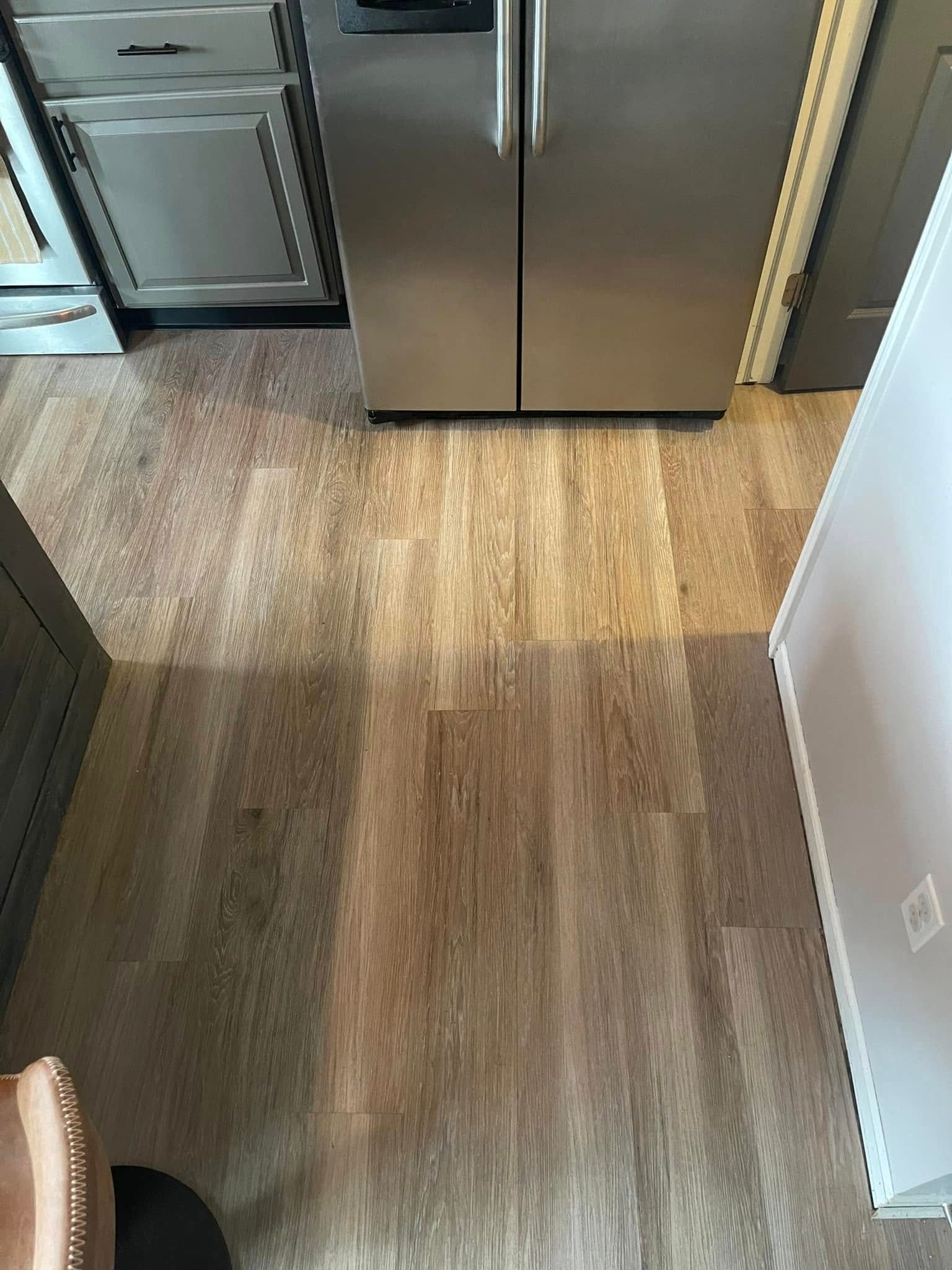 Wooden floor in a kitchen with a stainless steel refrigerator and cabinets.