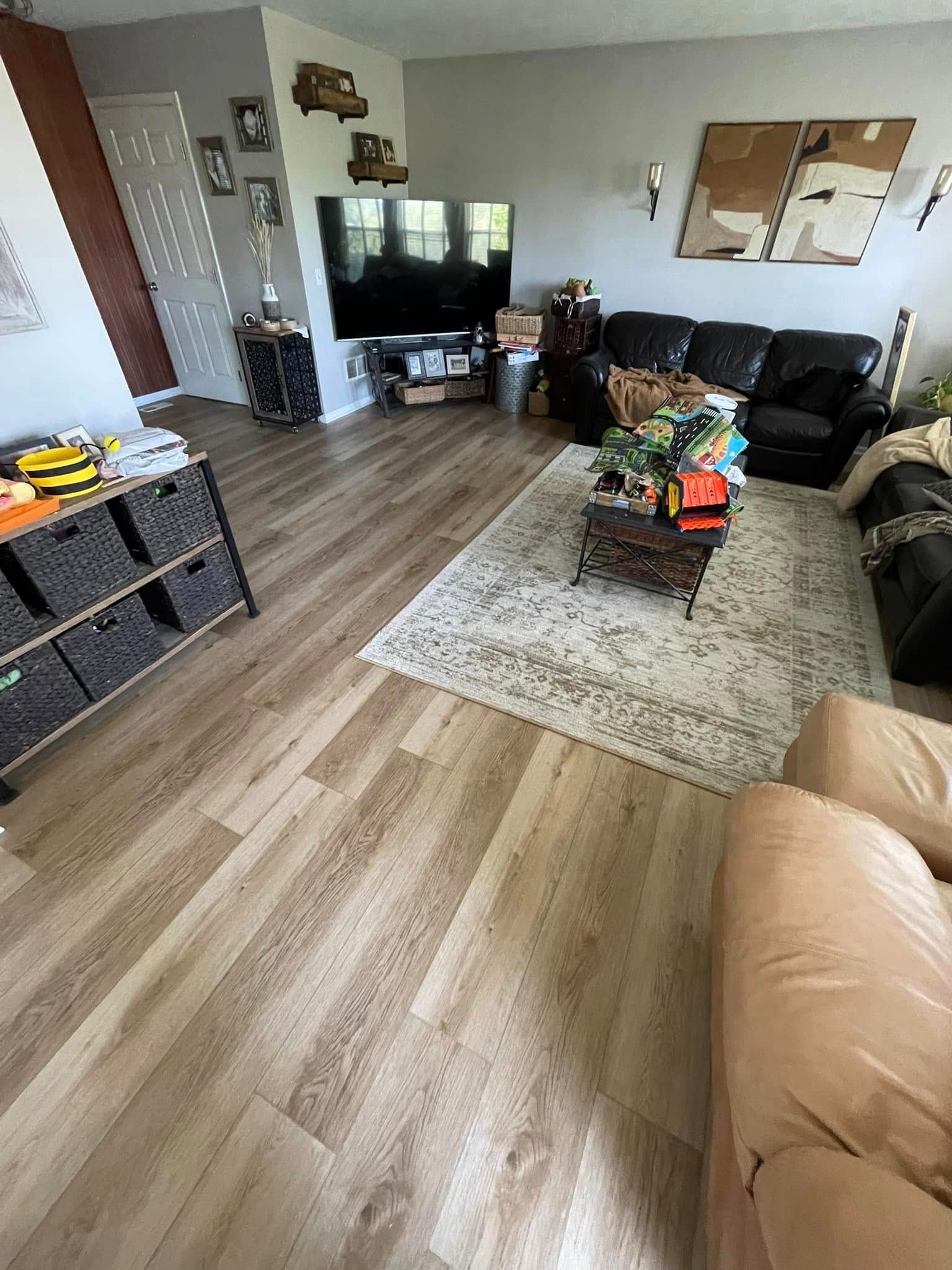 Living room with light wood floors, rug, and dark furniture. TV on the wall. Storage bins to the left.