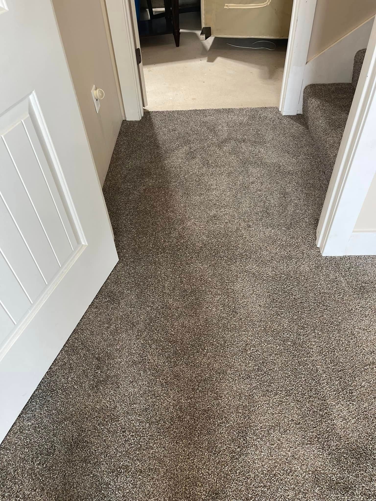 Hallway with brown speckled carpet, white door frames, and a glimpse into another room.