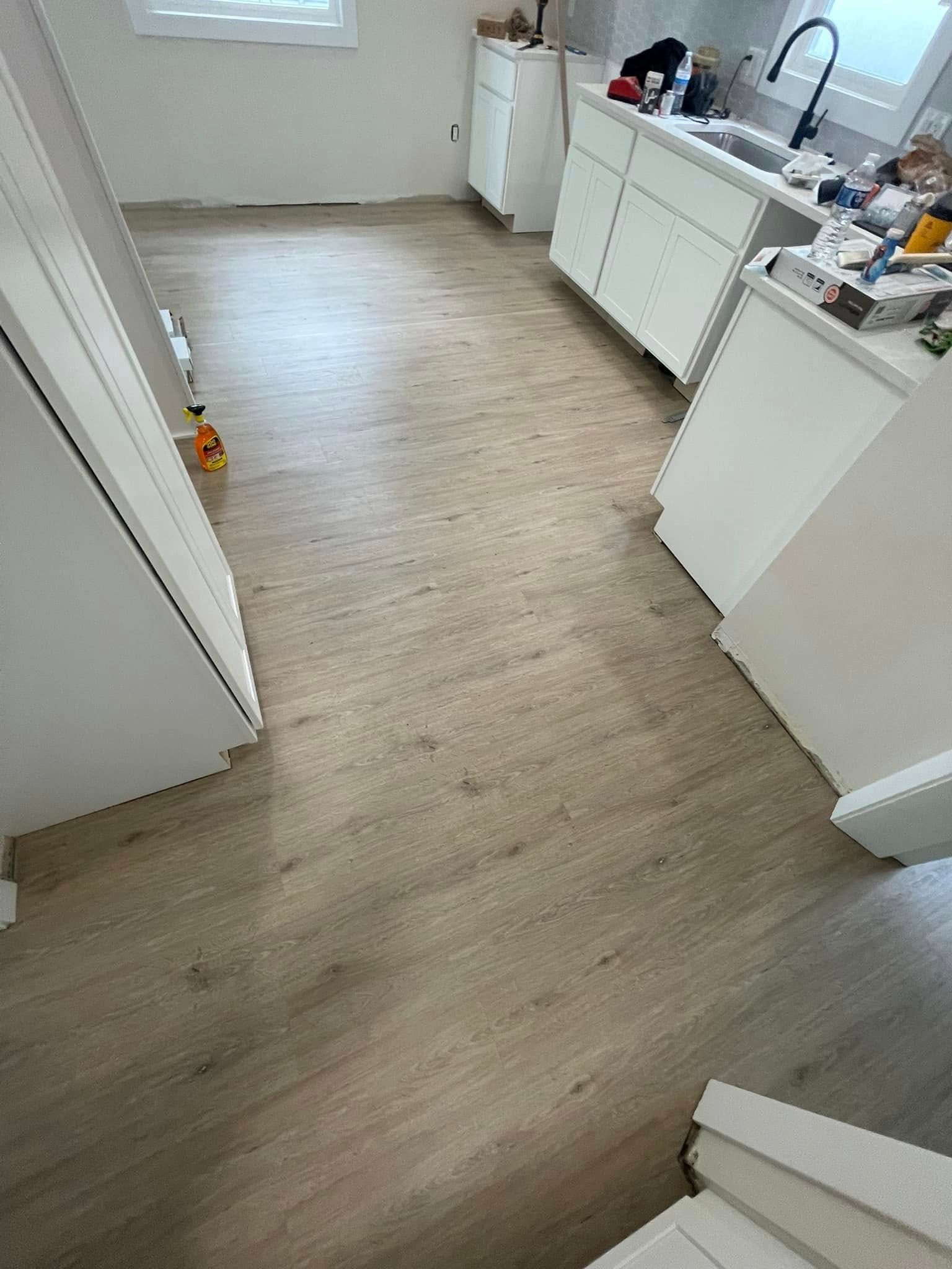 Kitchen with light wood-look flooring and white cabinetry under construction.