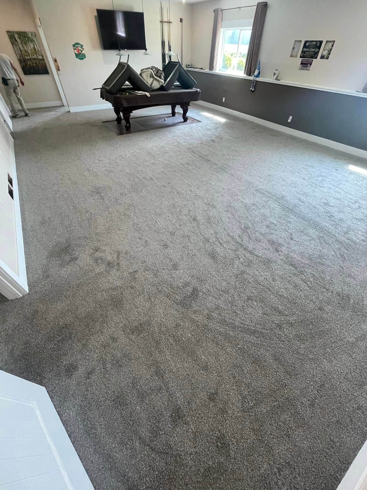 Spacious room with gray carpet, a pool table, and a dark wall. Bright light coming from a window.