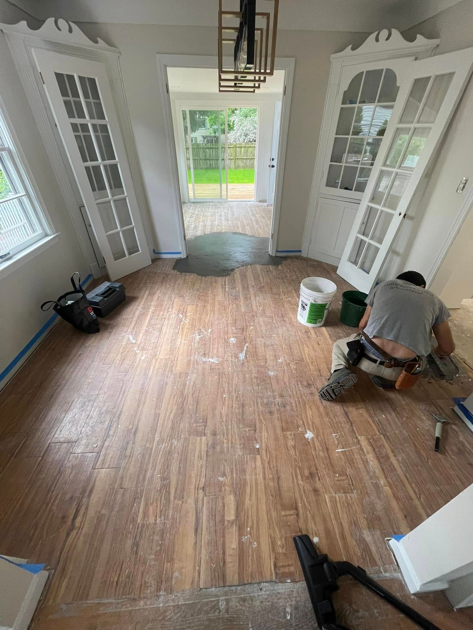 Renovating room with hardwood floor. A person kneels, doors open, and light streams in.