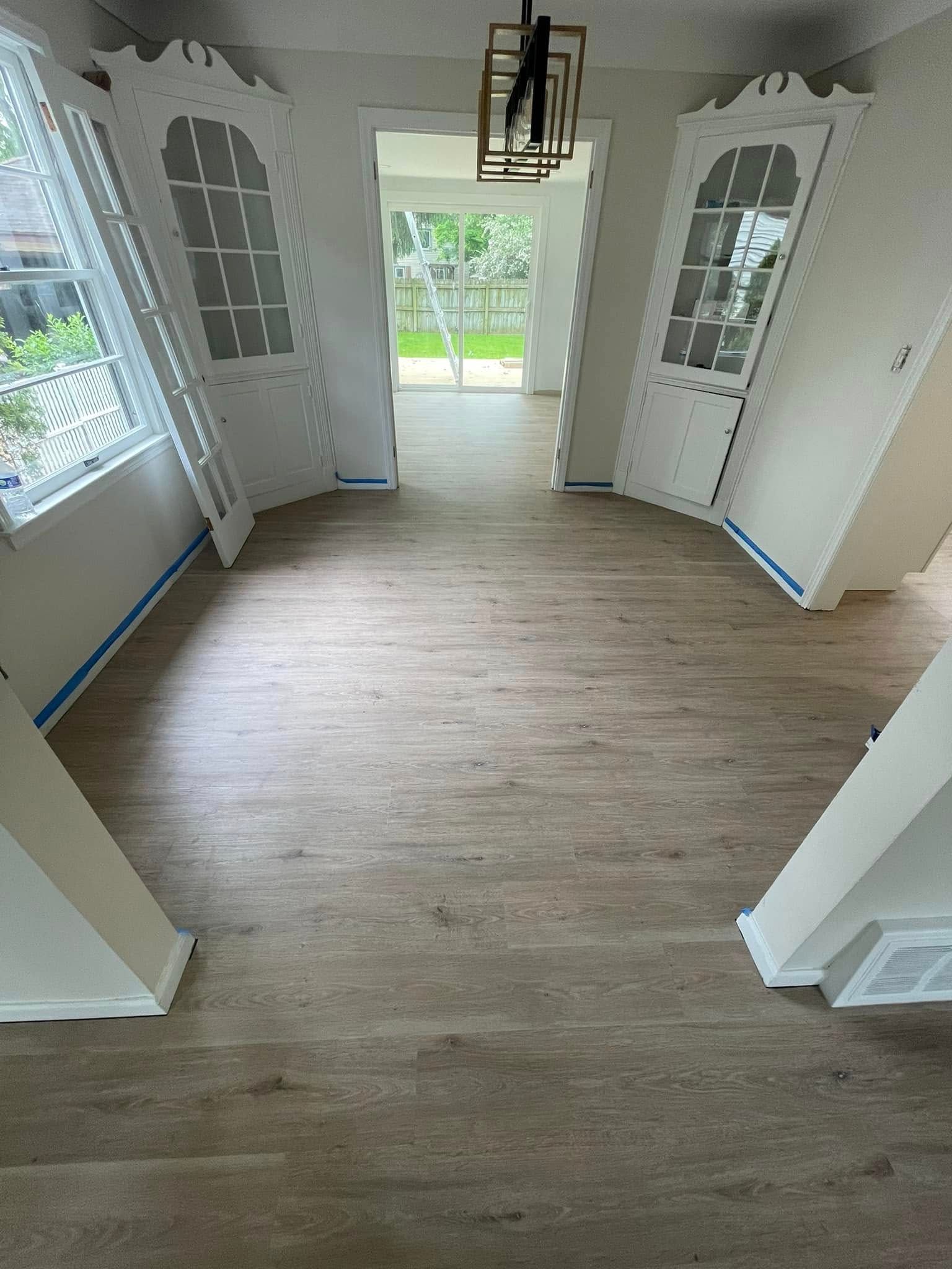 Interior view of a room with light wood flooring. White arched wall cabinets line the side walls, leading to an open doorway.