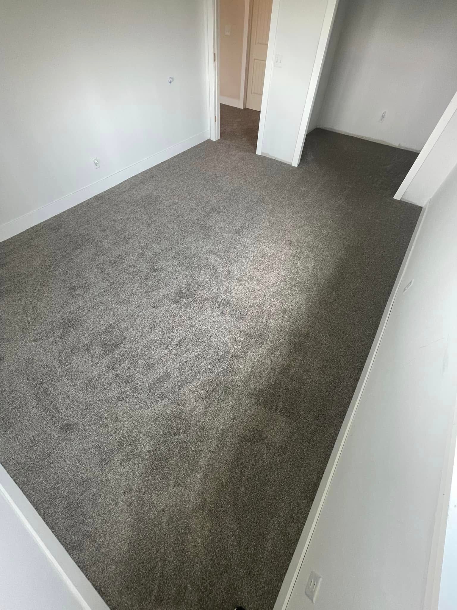 Room with new gray carpet, white walls, and an open doorway to another room.