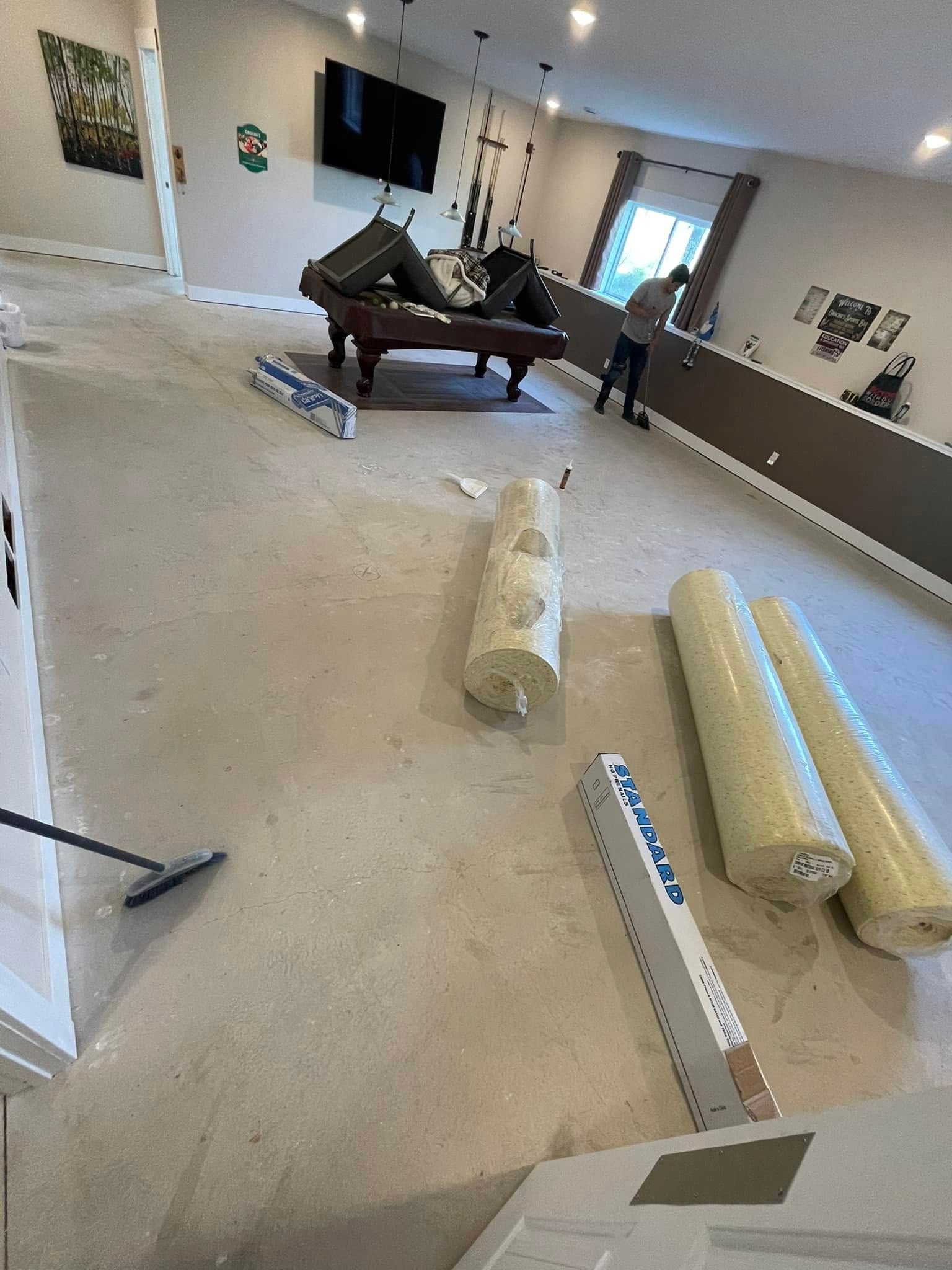 Interior view of a room with construction in progress: rolls of carpet and a person standing next to a wall.