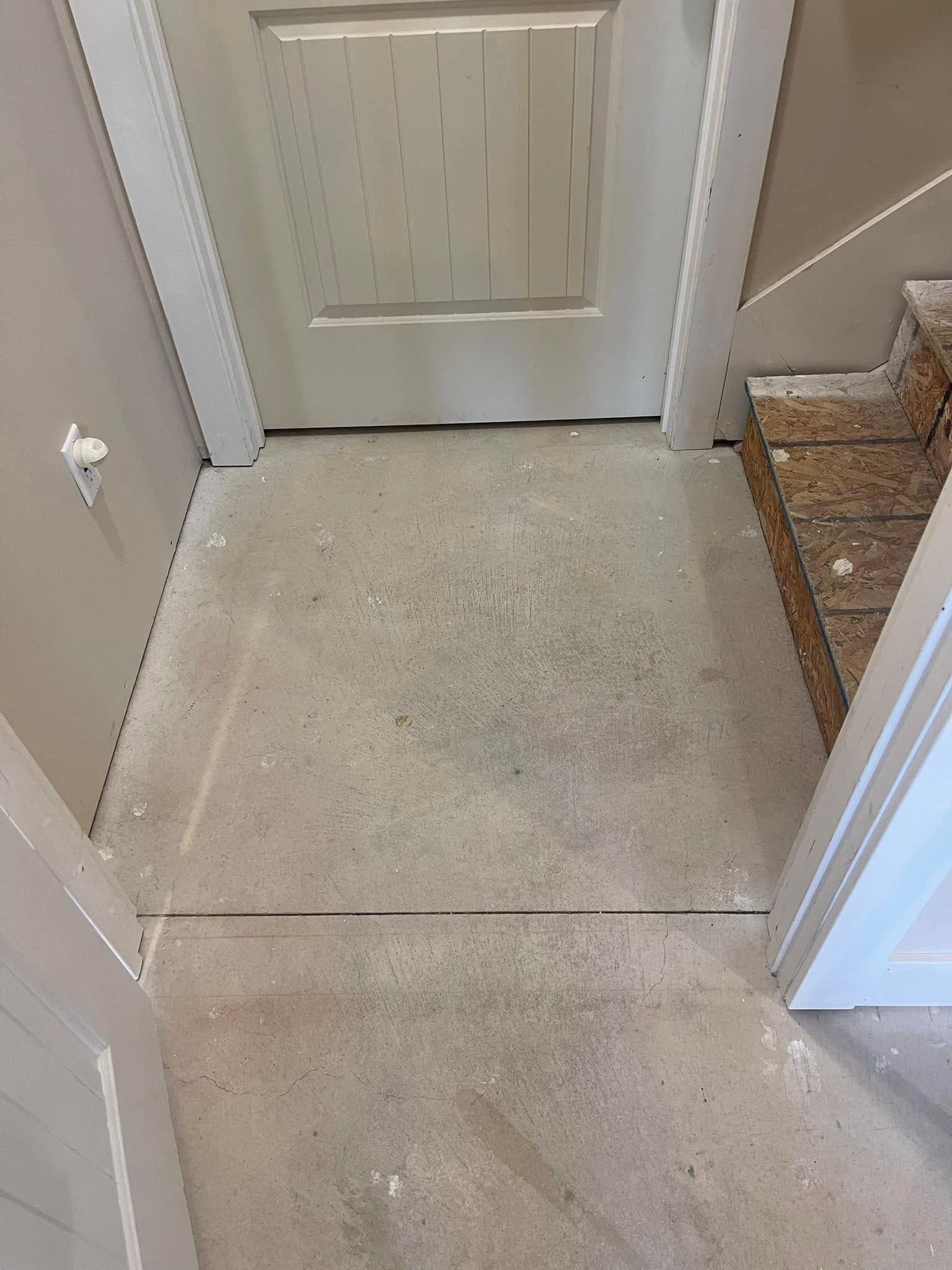 A door, floor, and stairs. The concrete floor has specks on it. White door trim, tan walls.