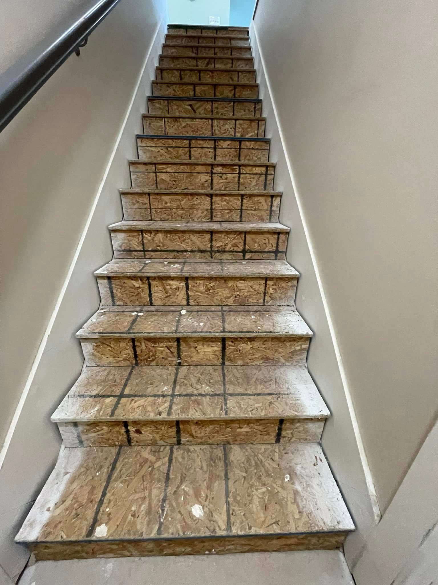 Staircase with exposed wood steps, beige walls, and a black handrail.