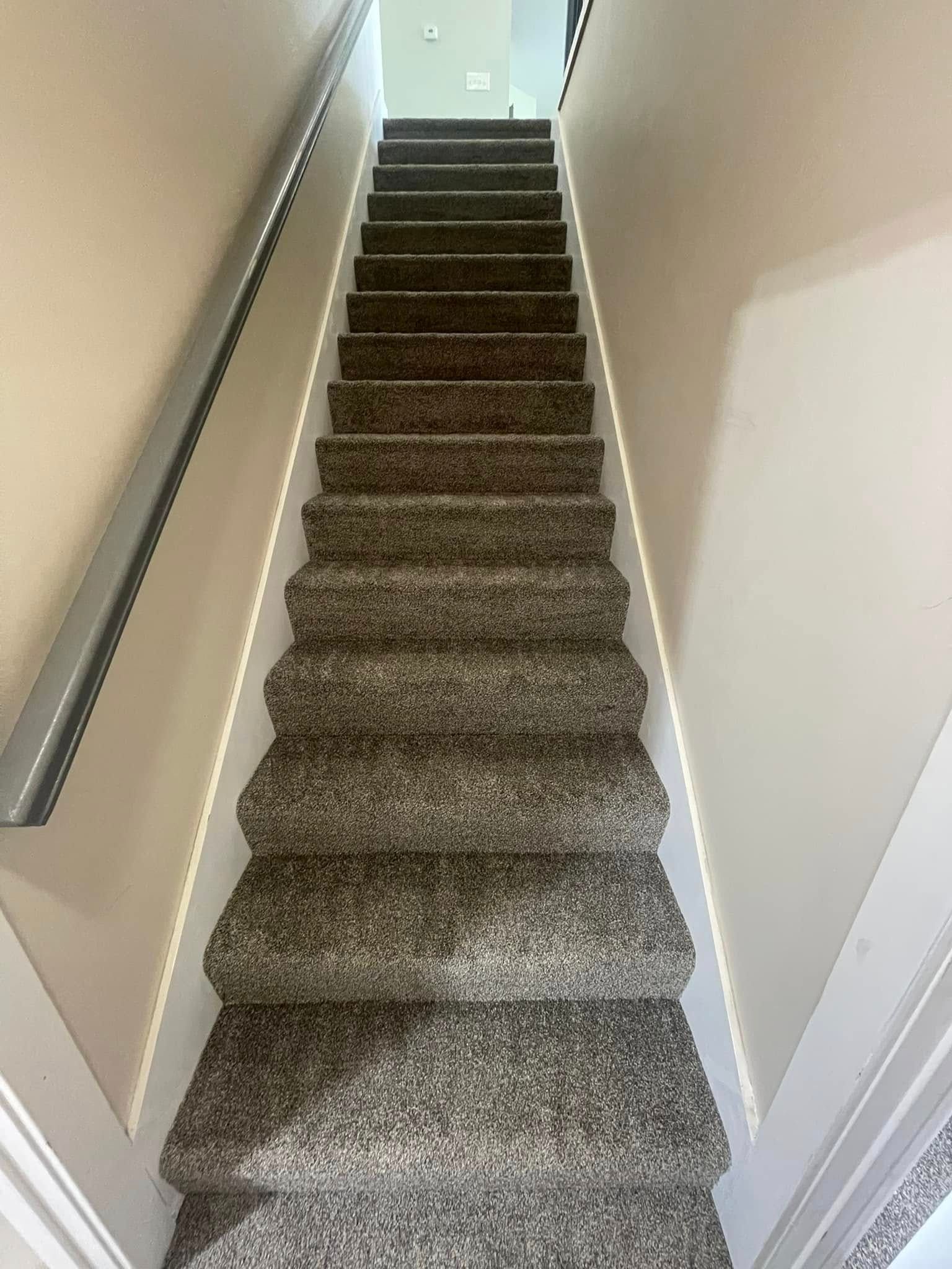 Staircase covered in speckled gray carpet, with a handrail on the left.