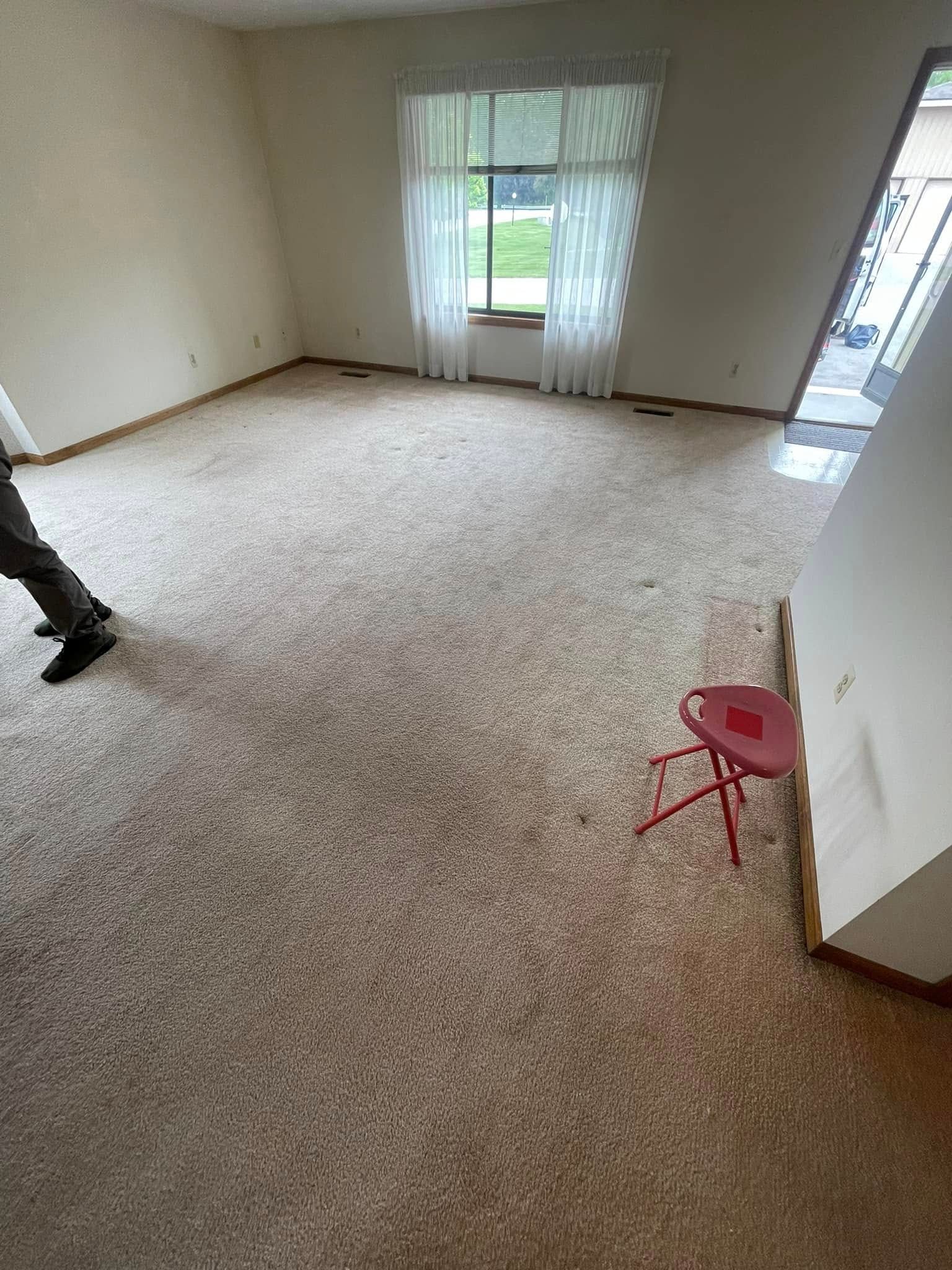 Empty room with tan carpet, a window with curtains, and a red stool.