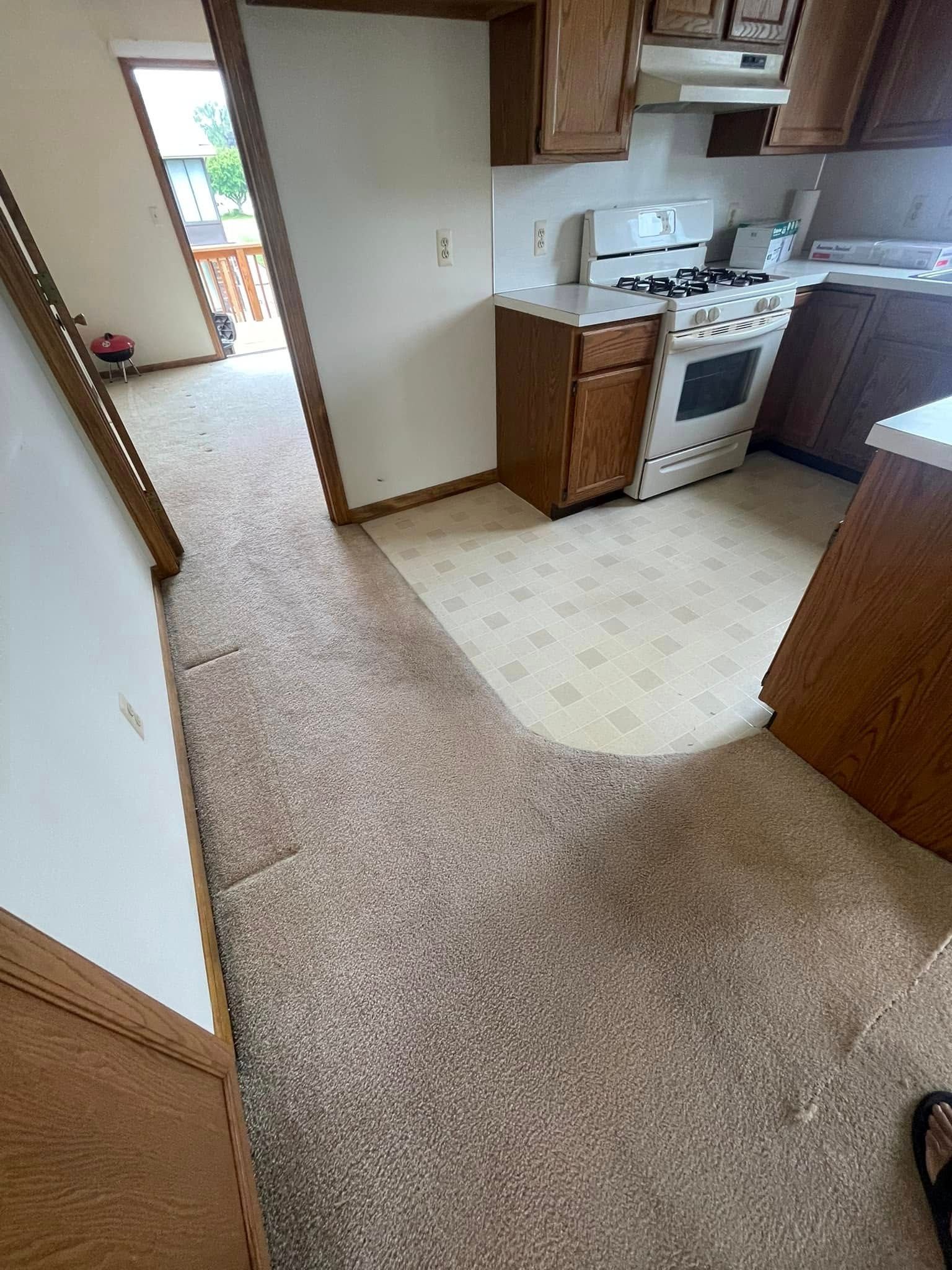 Interior view: kitchen with wood cabinets, stove, and a carpeted hallway leading to a doorway.