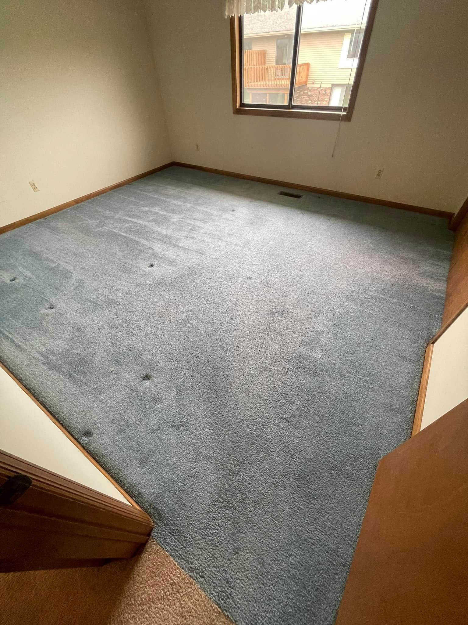 Empty room with blue carpet, window, and wood trim.