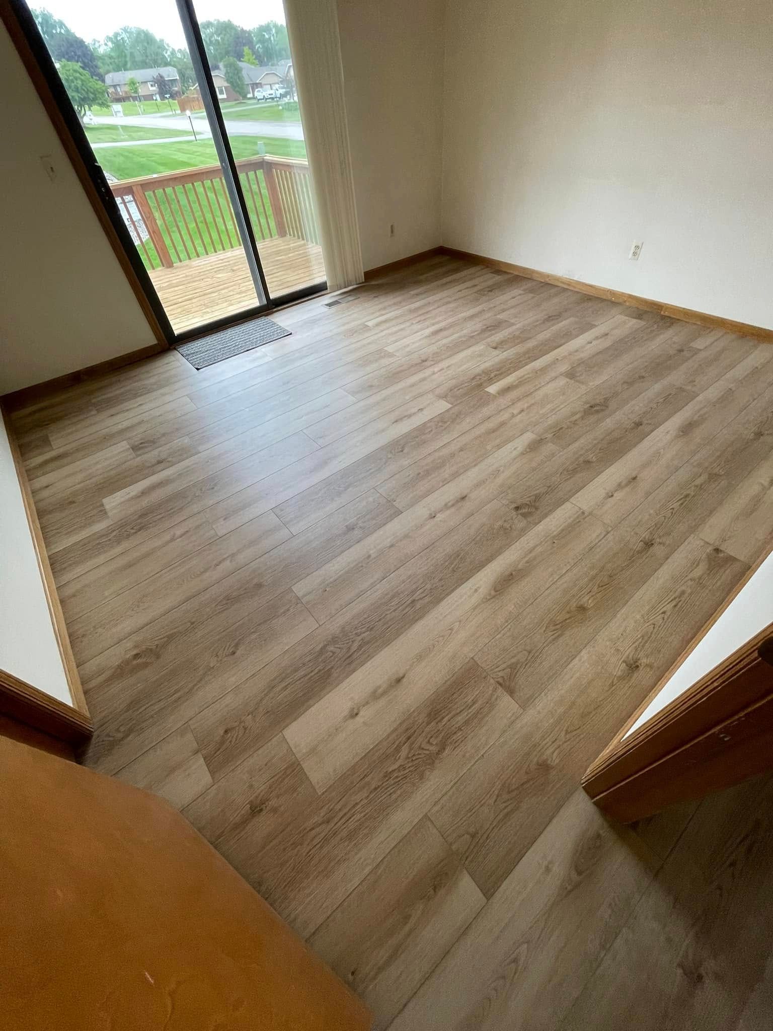 Empty room with new wood-look flooring, sliding glass door leading to a deck, and white walls.